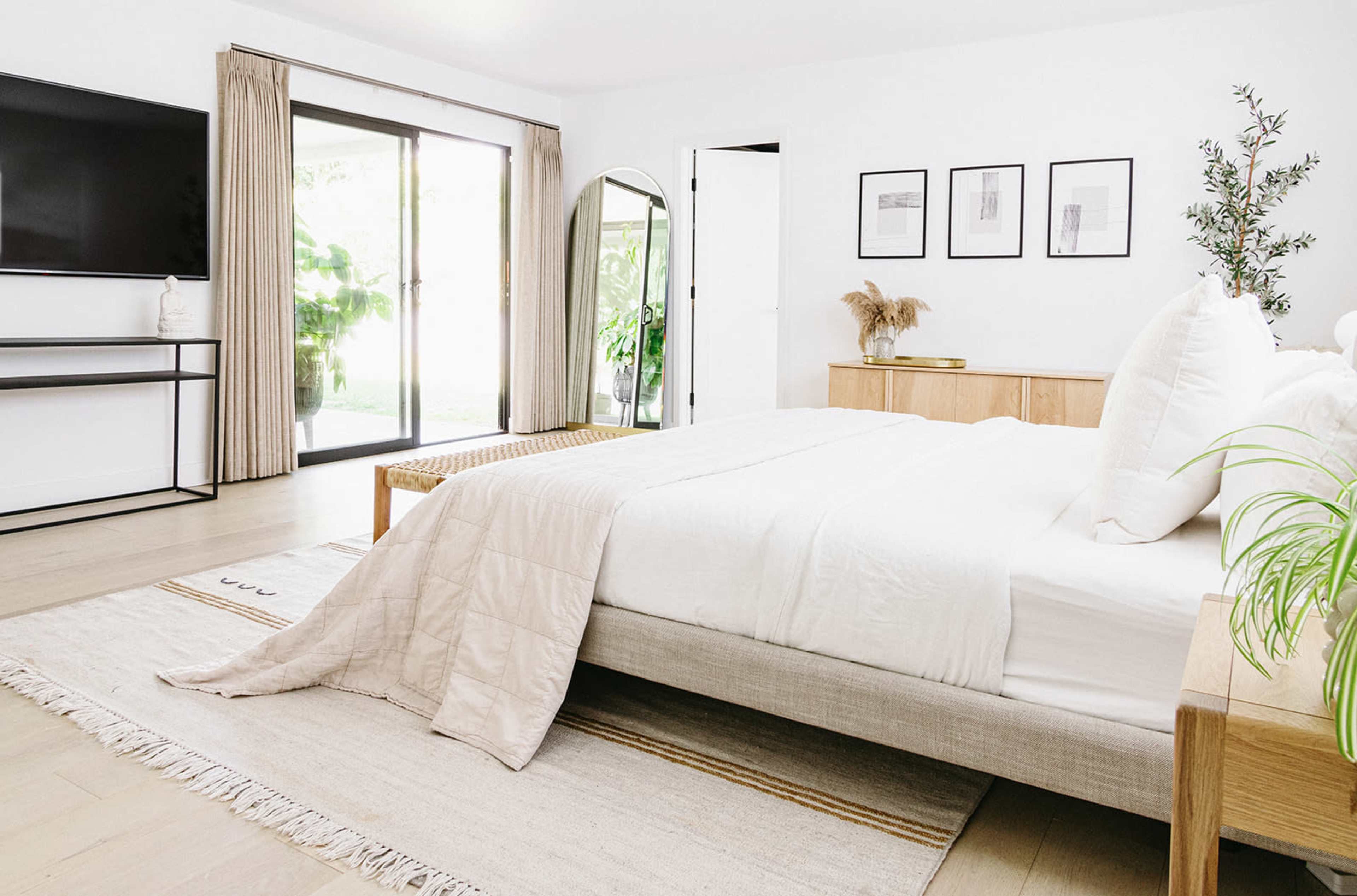 A modern bedroom featuring a large bed with white bedding, a flat-screen TV mounted on a wall, and large sliding glass doors that open to a patio.