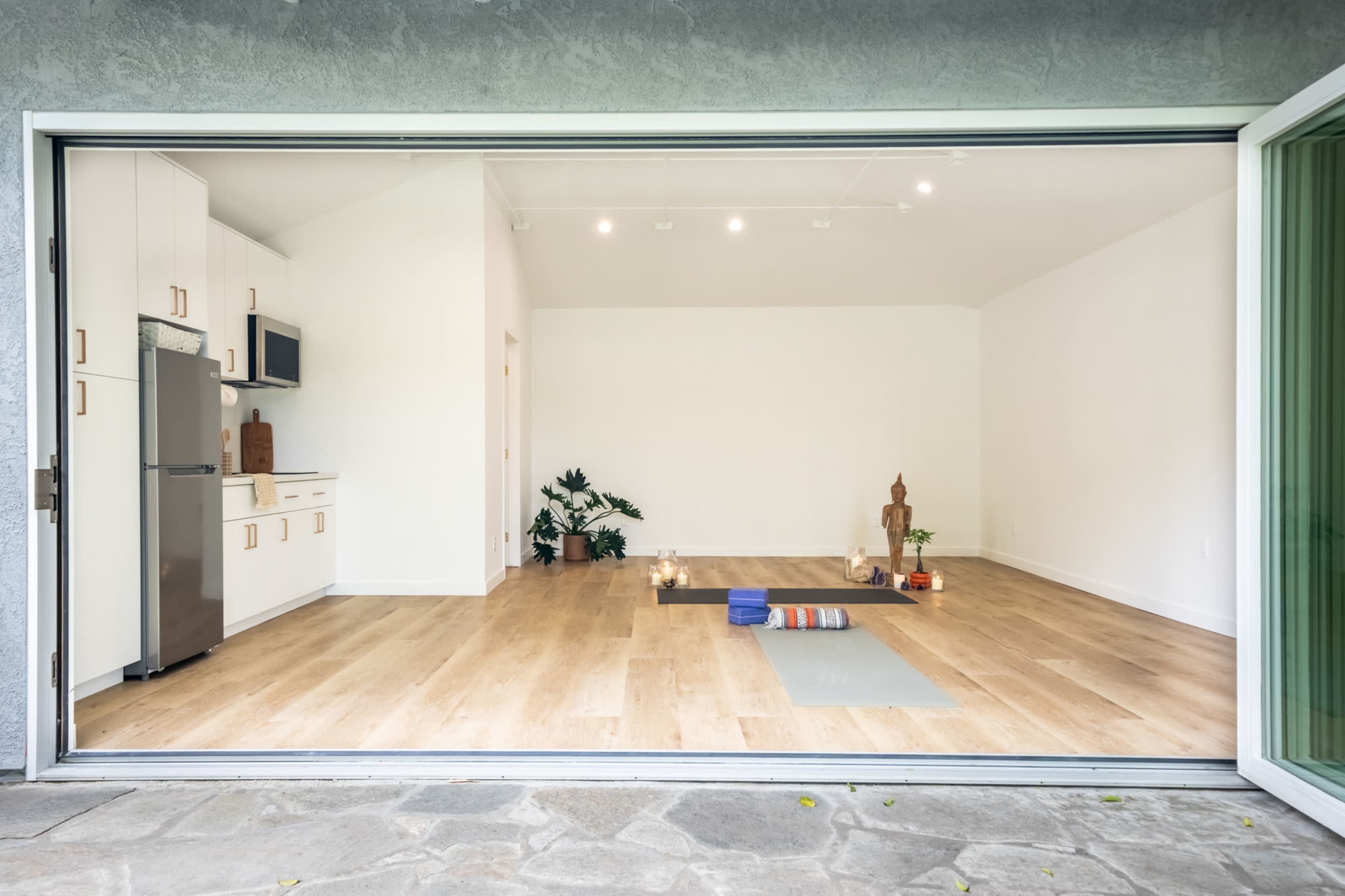 A minimalist kitchen and a spacious, empty room with wooden floors are visible through large sliding glass doors.