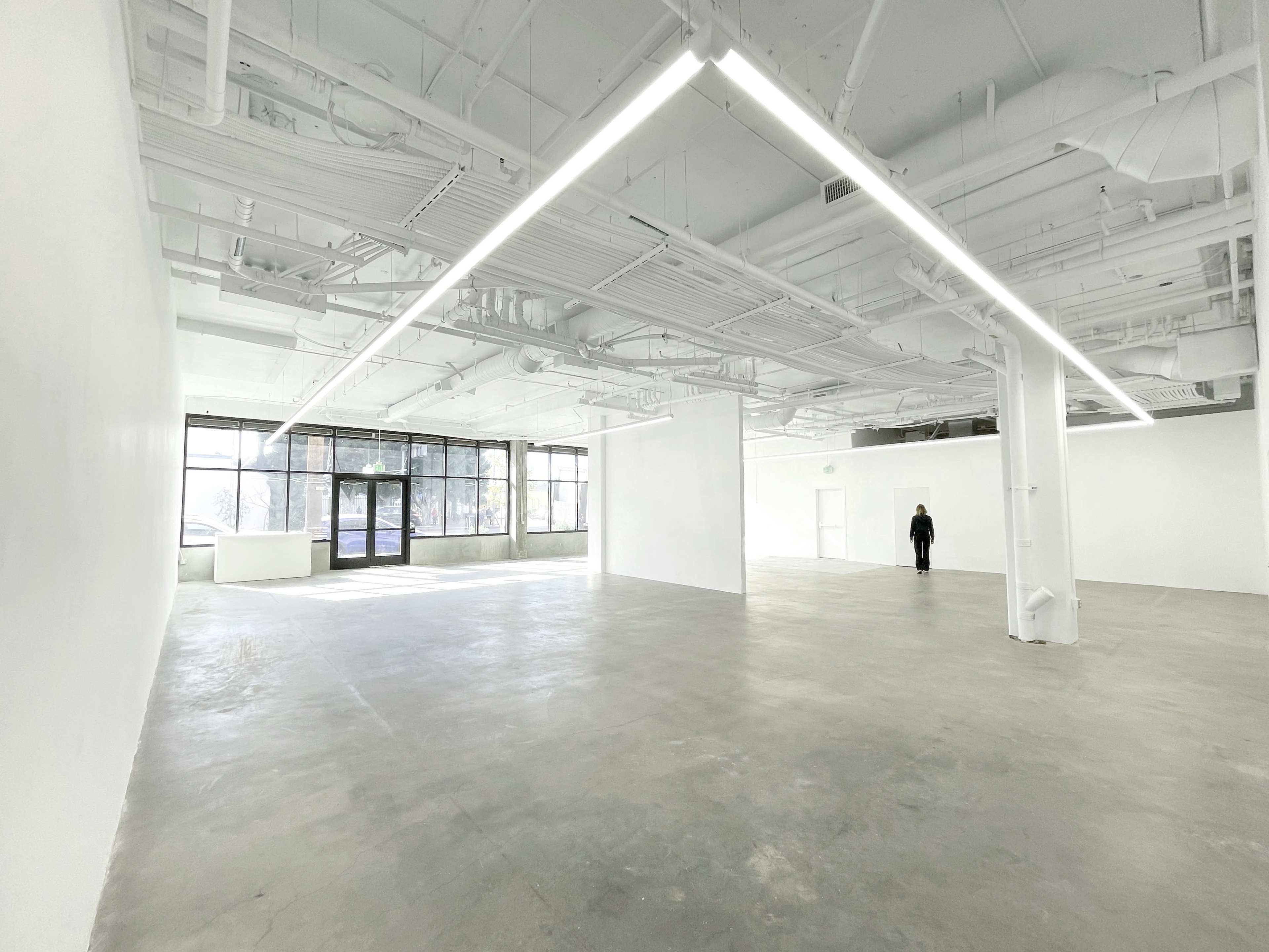 An empty, well-lit room with gray concrete flooring and large windows on one side.