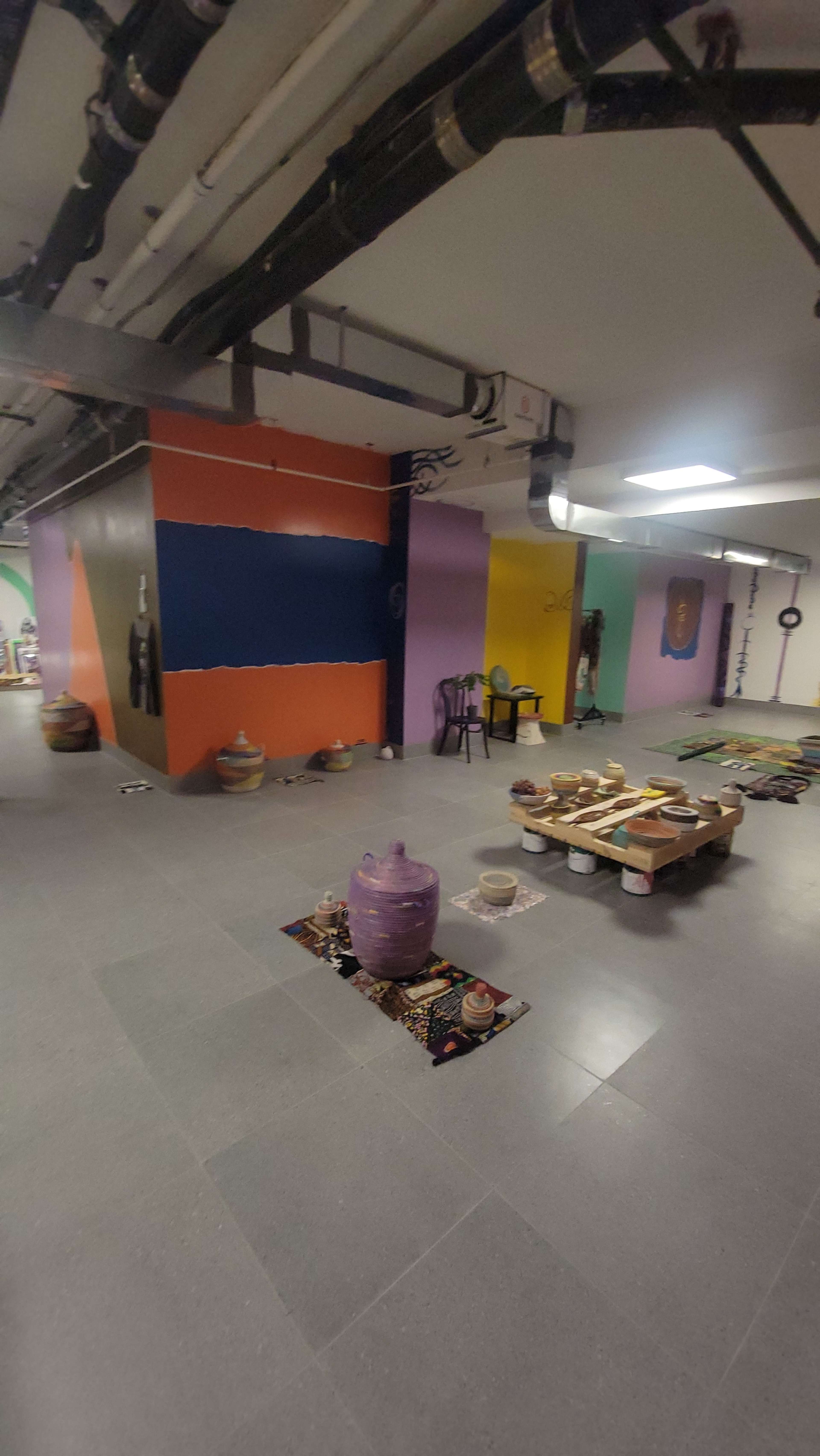 The scene shows a spacious basement area with colorful walls, pottery items scattered around, and a setup of tables featuring various objects.