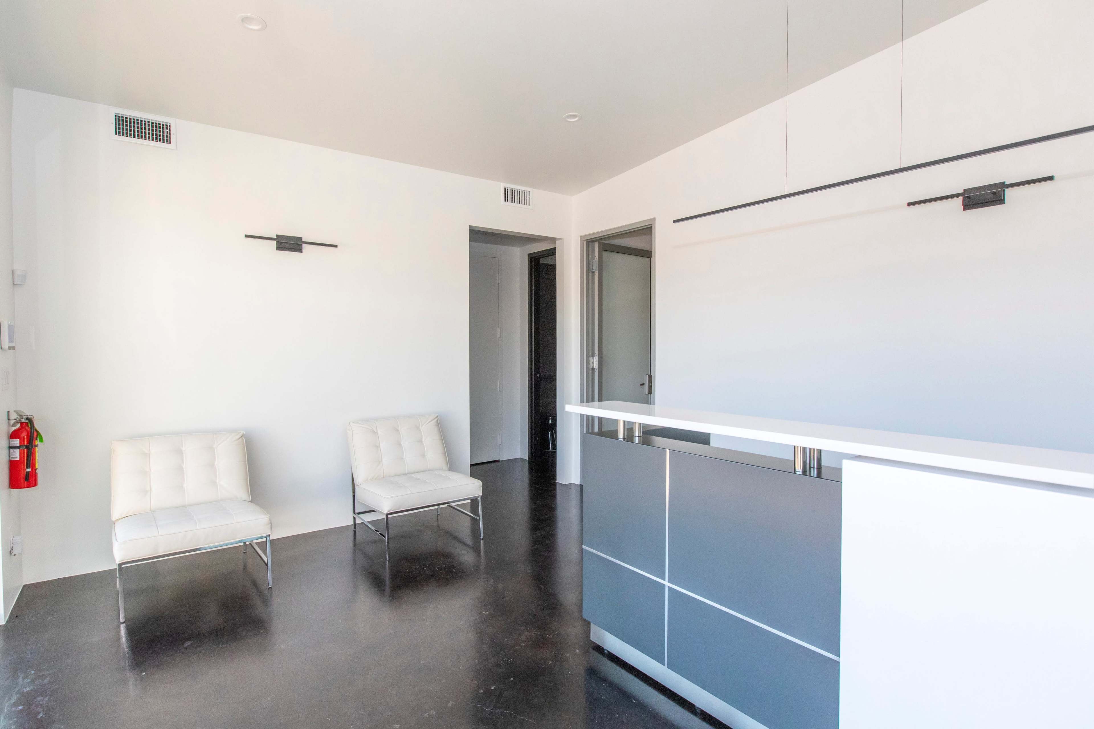 A modern office reception area featuring two white chairs and a sleek reception desk against a minimalist background.