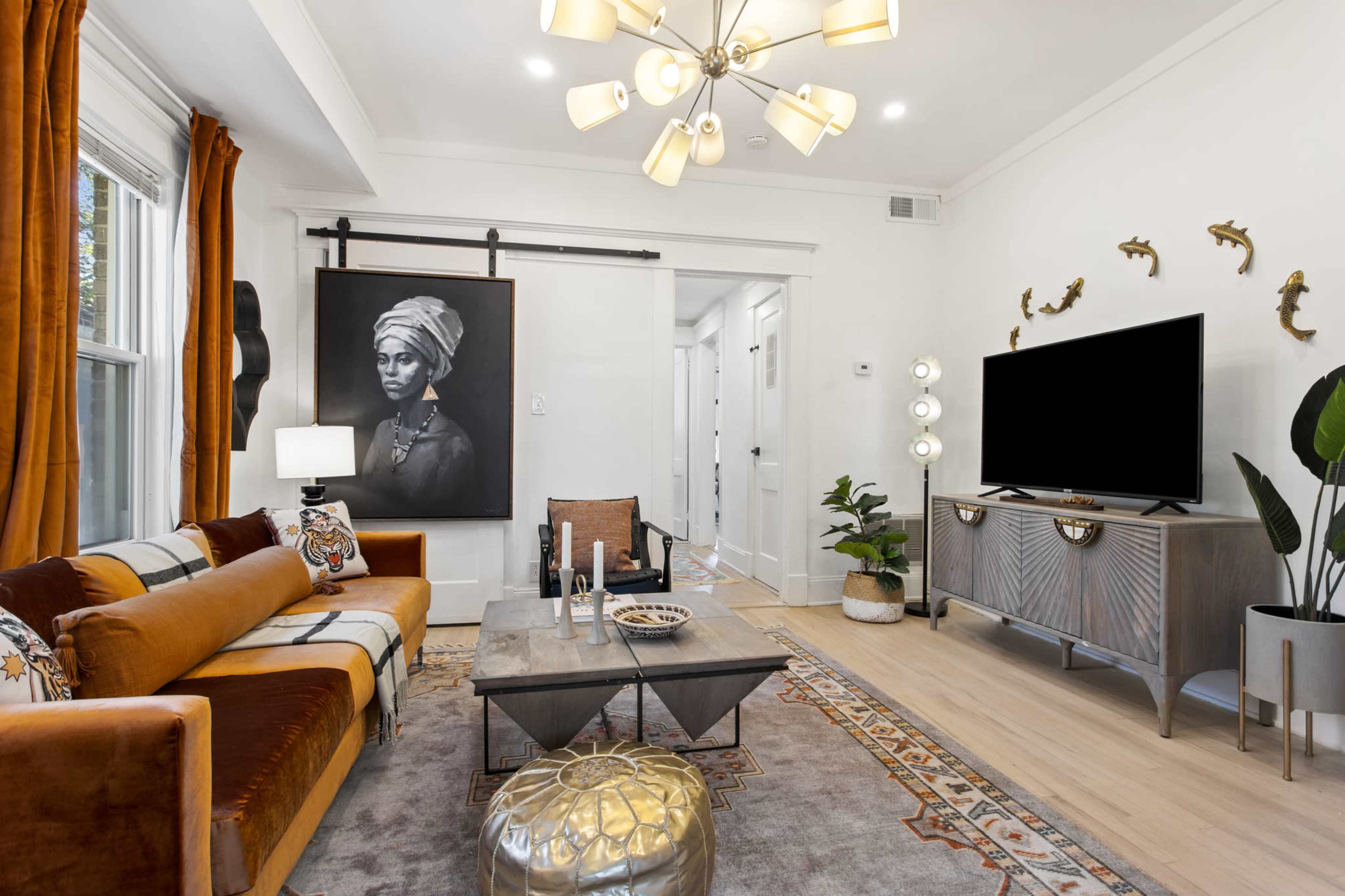 A modern living room featuring a large painting of a woman, a stylish sofa, a coffee table, and a television on a console.