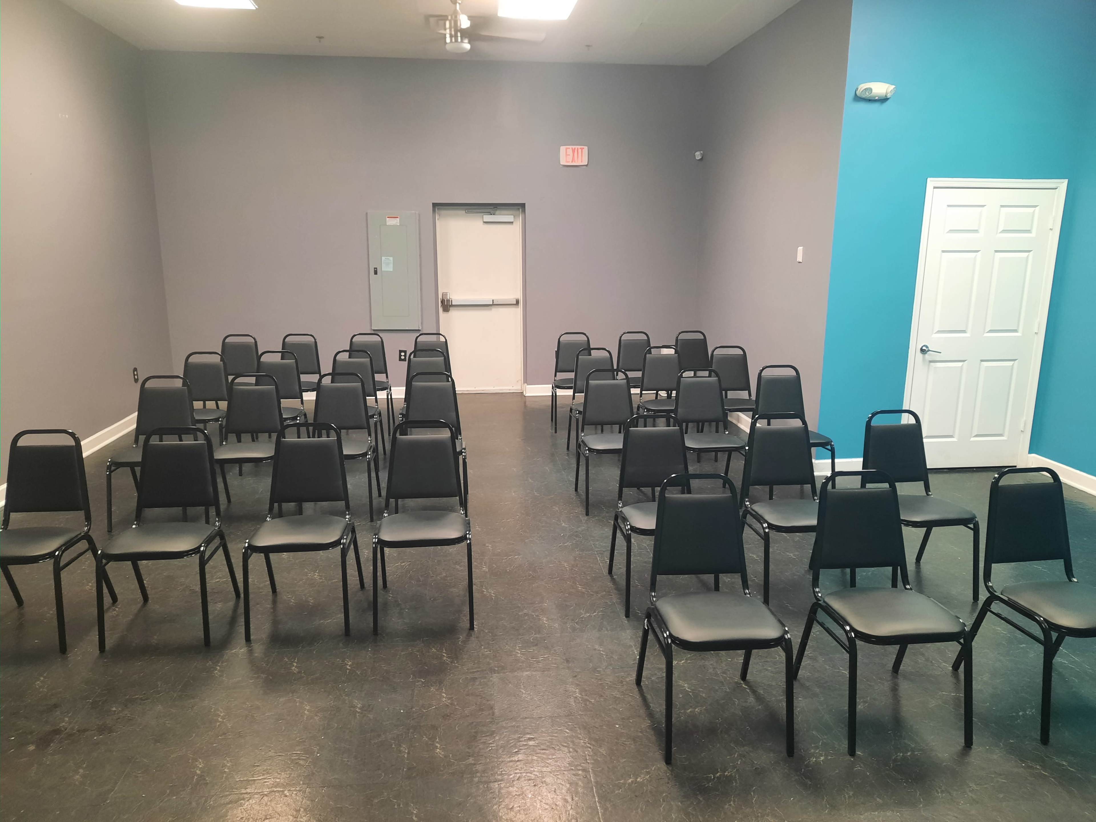 A room with a set of neatly arranged black chairs facing a door at the back.
