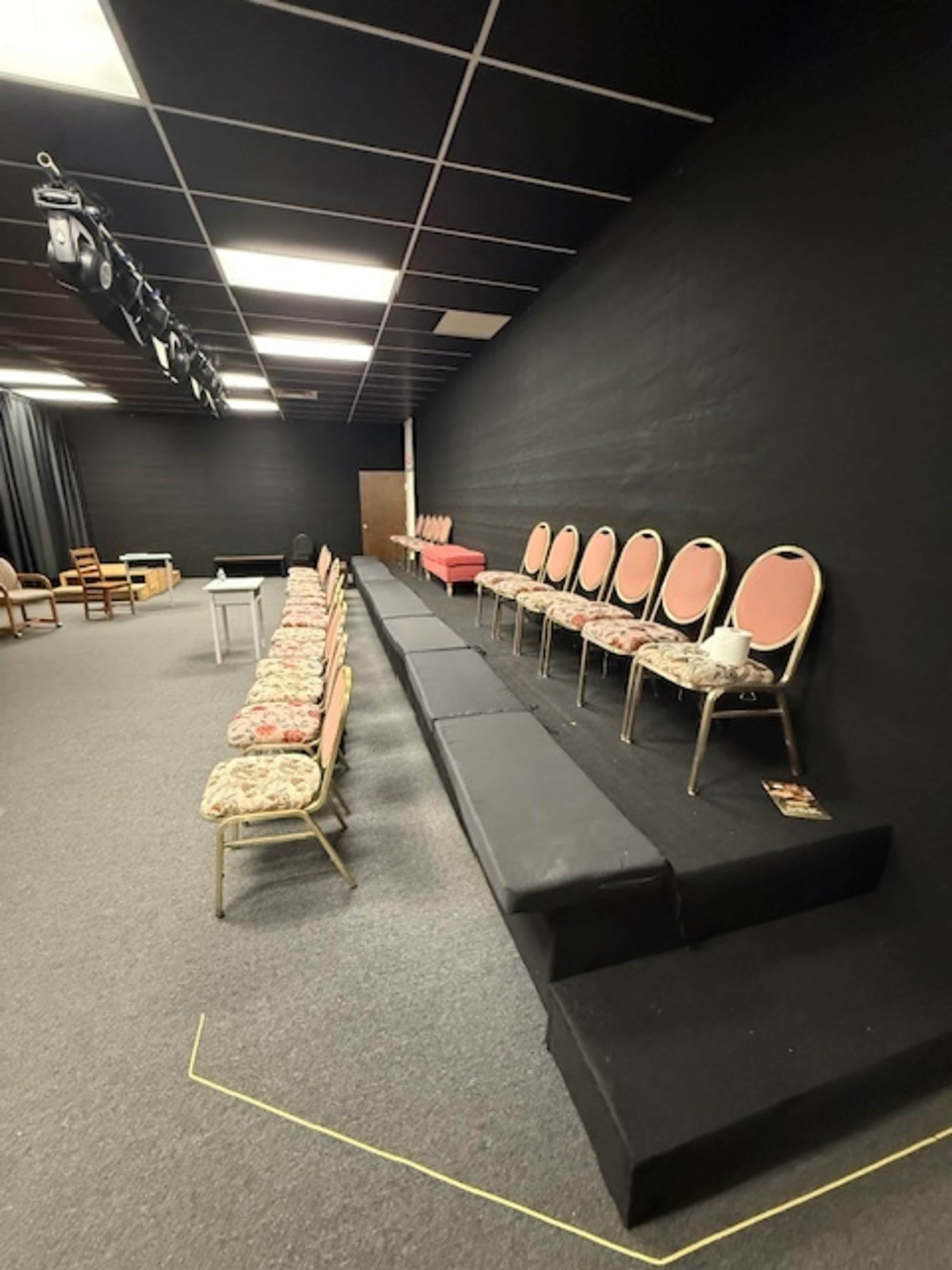 The image shows a theater-like setup with rows of upholstered chairs arranged on a raised platform in a dimly lit room.