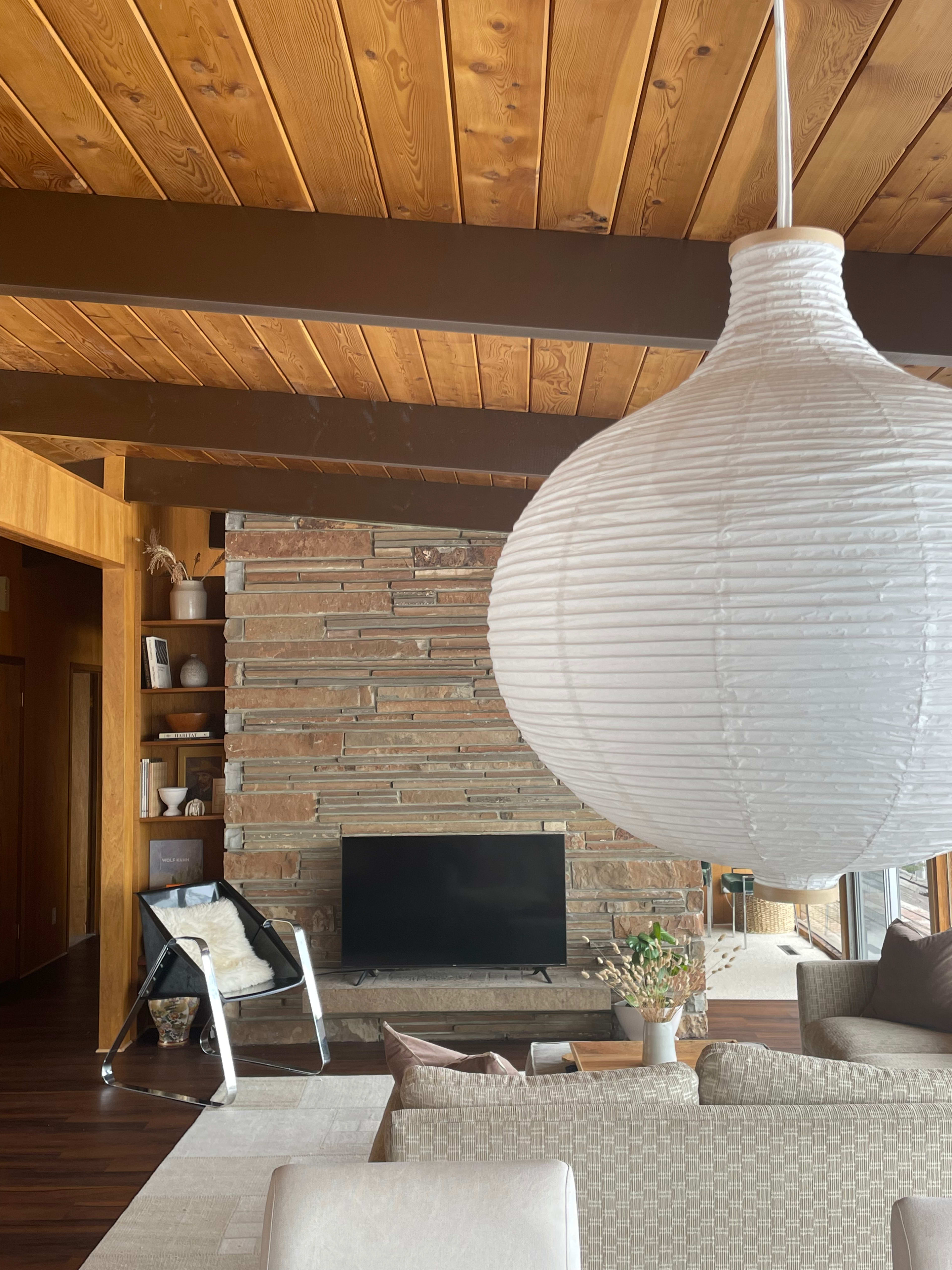 The scene features a modern living room with a stone fireplace, a television, a large hanging light fixture, and a cozy seating area.
