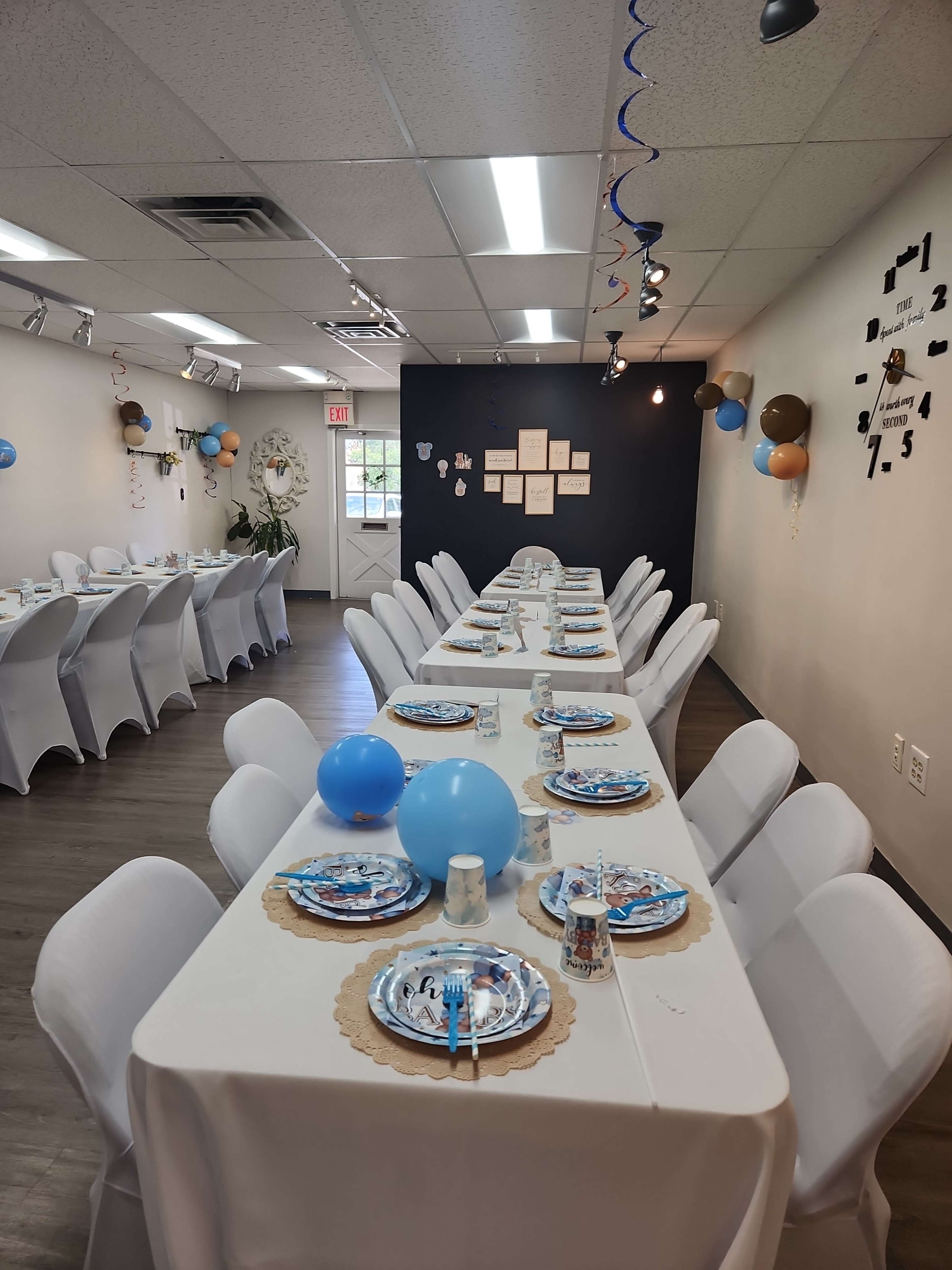 The image shows a decorated event space with tables set for a celebration, featuring white tablecloths, themed plates, and blue balloons.