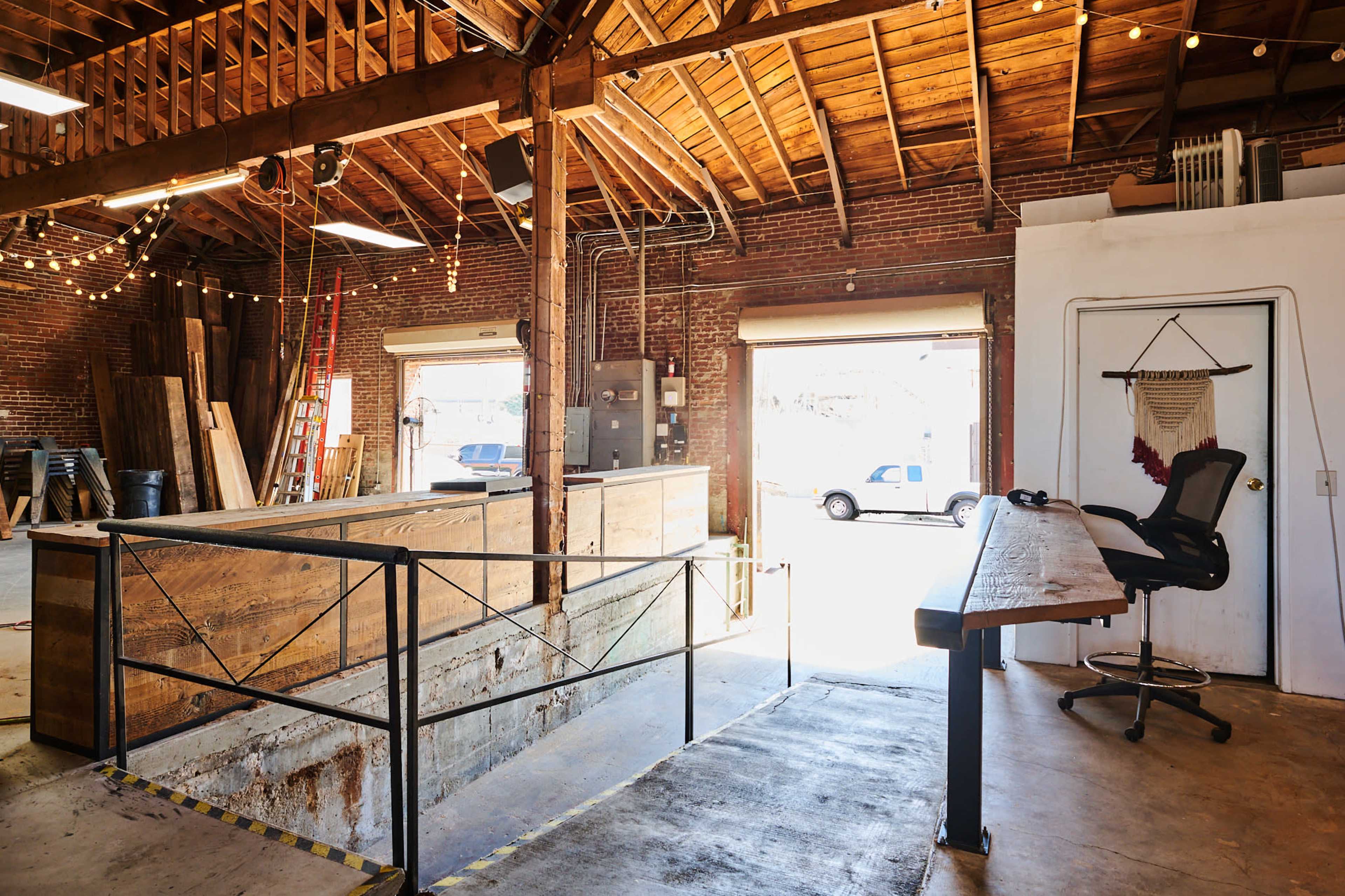 An open warehouse space with exposed wood beams, large entry doors, and a workbench overlooking a loading area.