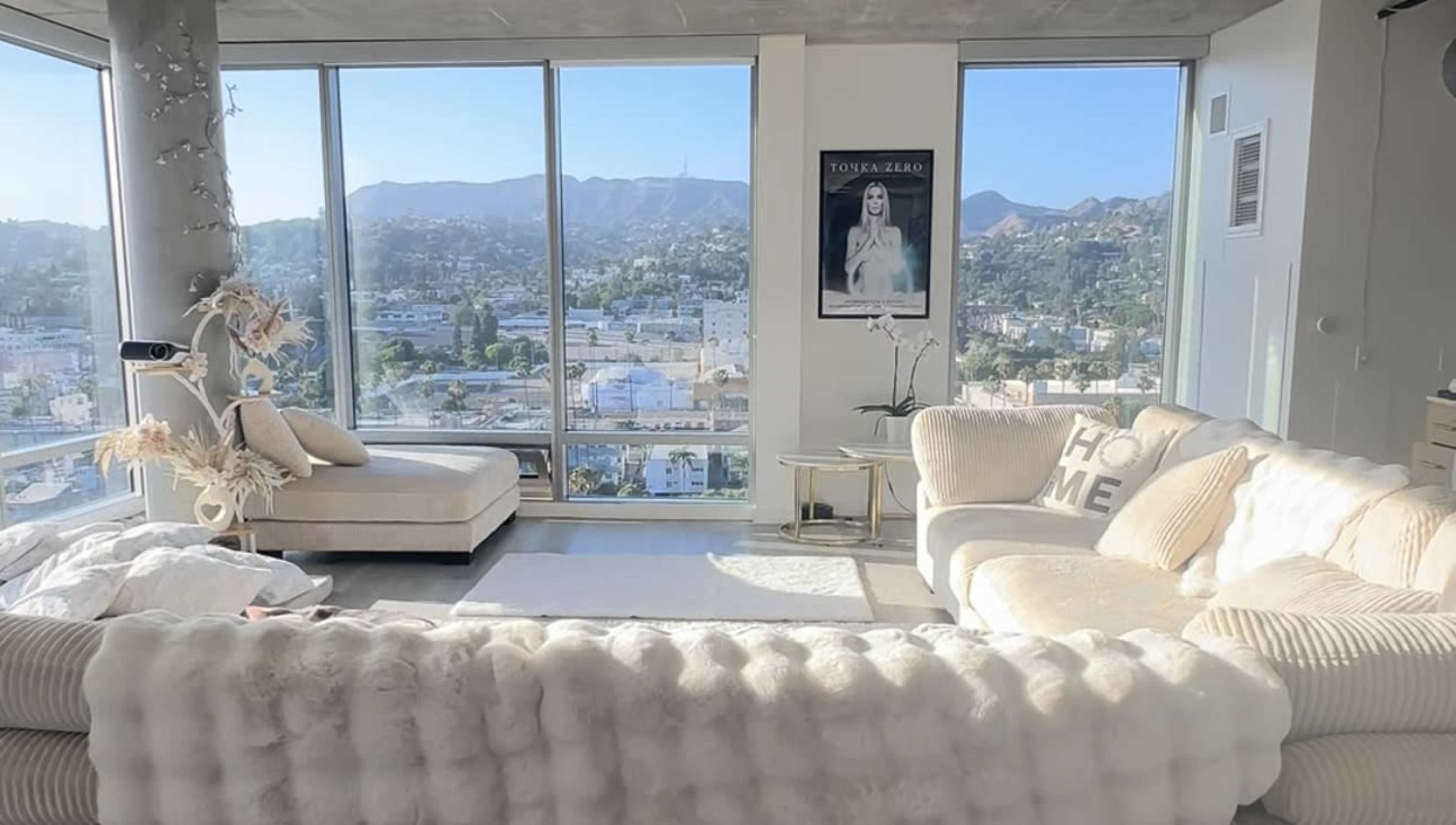 A bright living room features a large sectional couch, a chaise lounge, and large windows showcasing a mountainous cityscape.