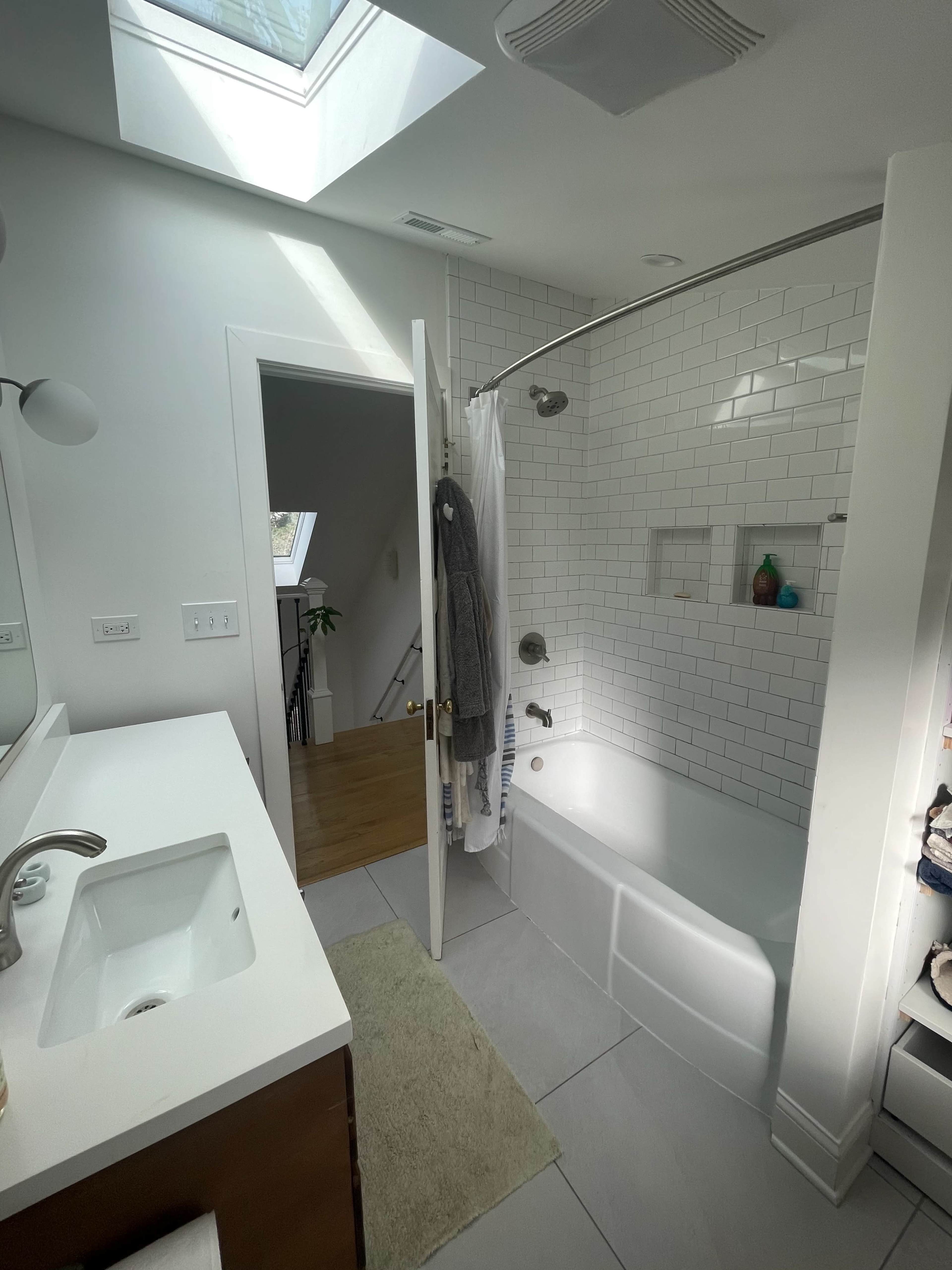 The bathroom features a bathtub with a glass shower door, a skylight, and a doorway leading to a staircase.