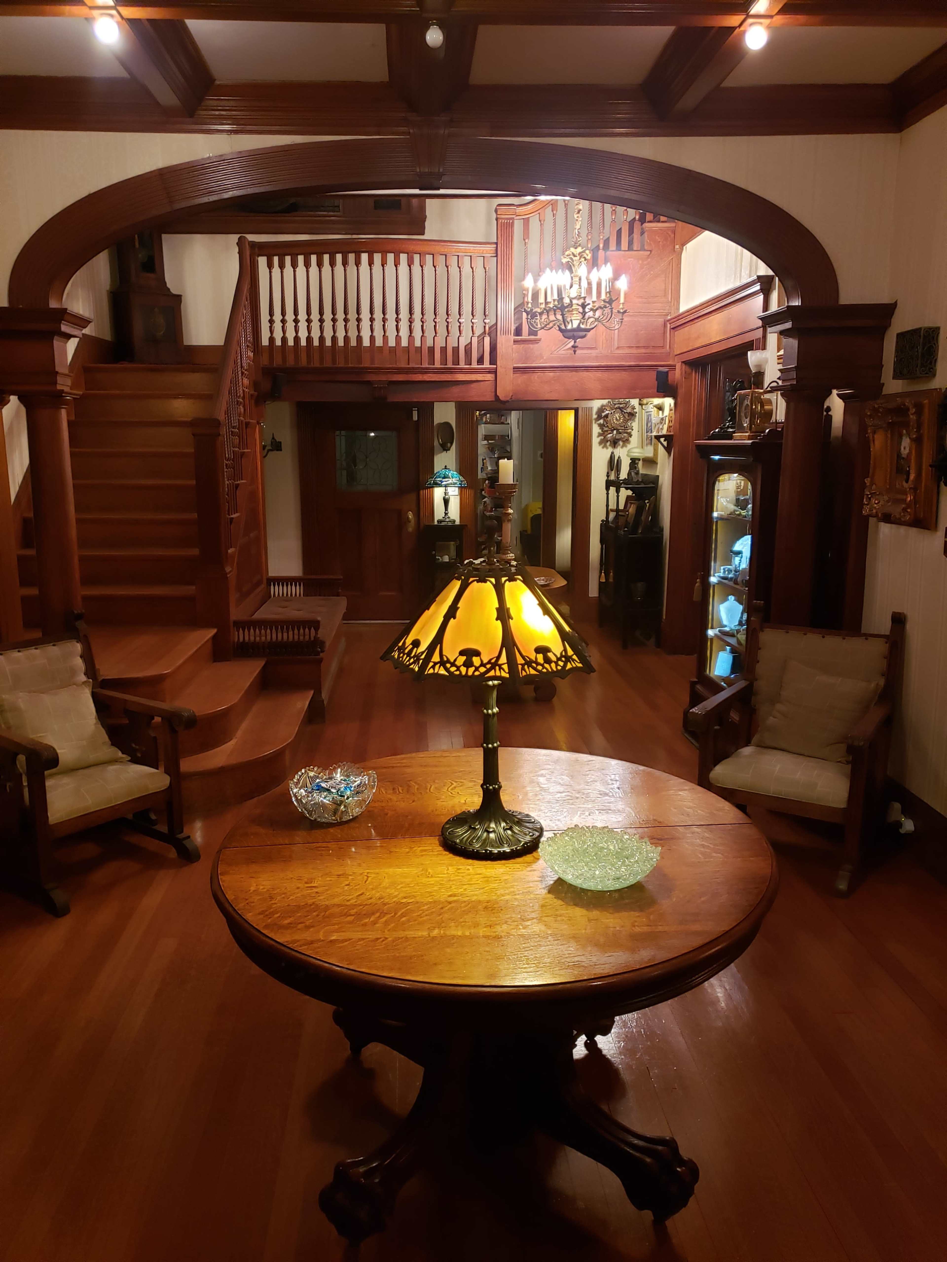 A spacious entryway featuring a round wooden table with a lamp, two upholstered chairs, and a staircase leading to the upper level.