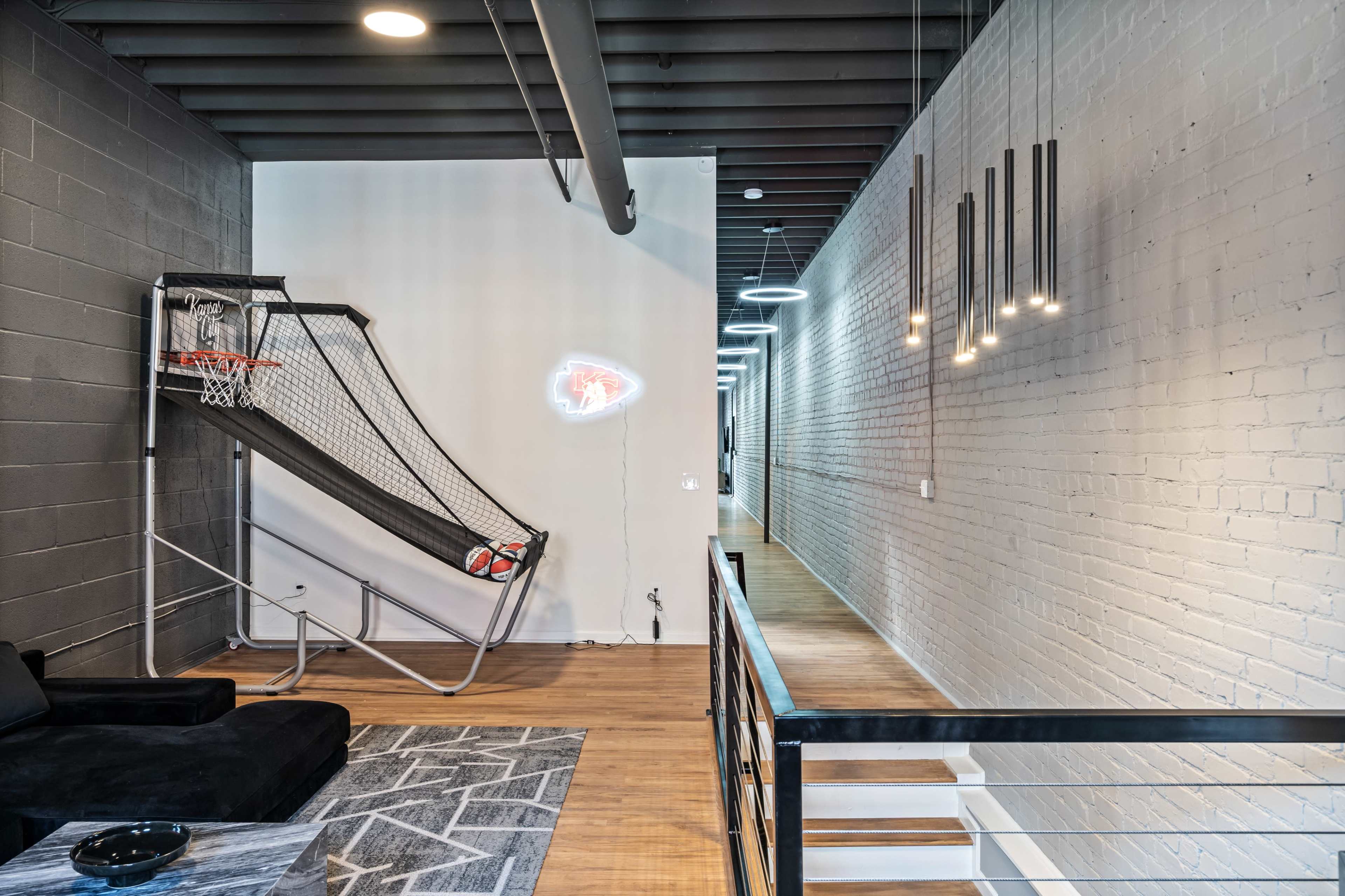 The image shows a modern interior space featuring a basketball hoop, a dark sofa, and a well-lit hallway with pendant lights.