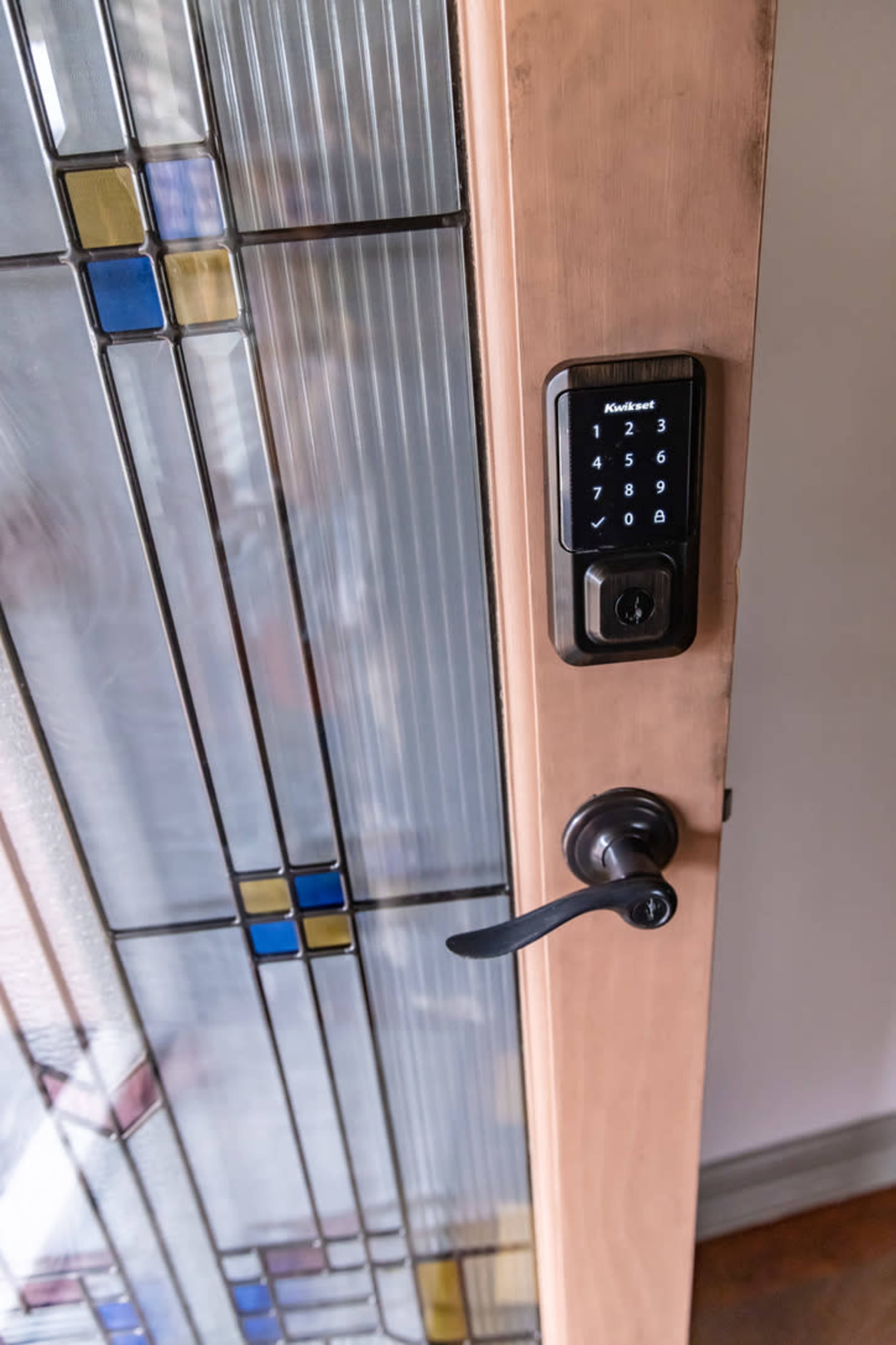A wooden door with a glass panel featuring colored designs, equipped with a digital keypad lock on the right side.