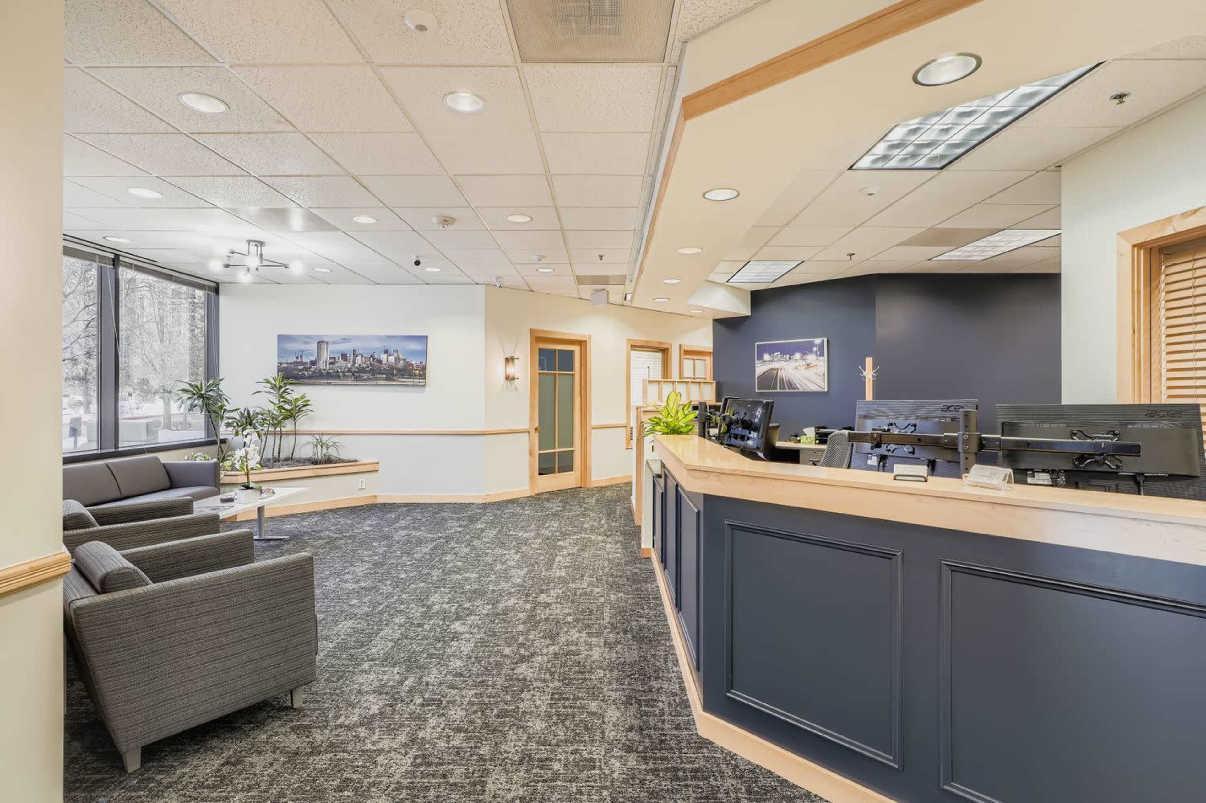 The image shows a modern office reception area with a seating arrangement, a front desk, and decorative artwork on the walls.
