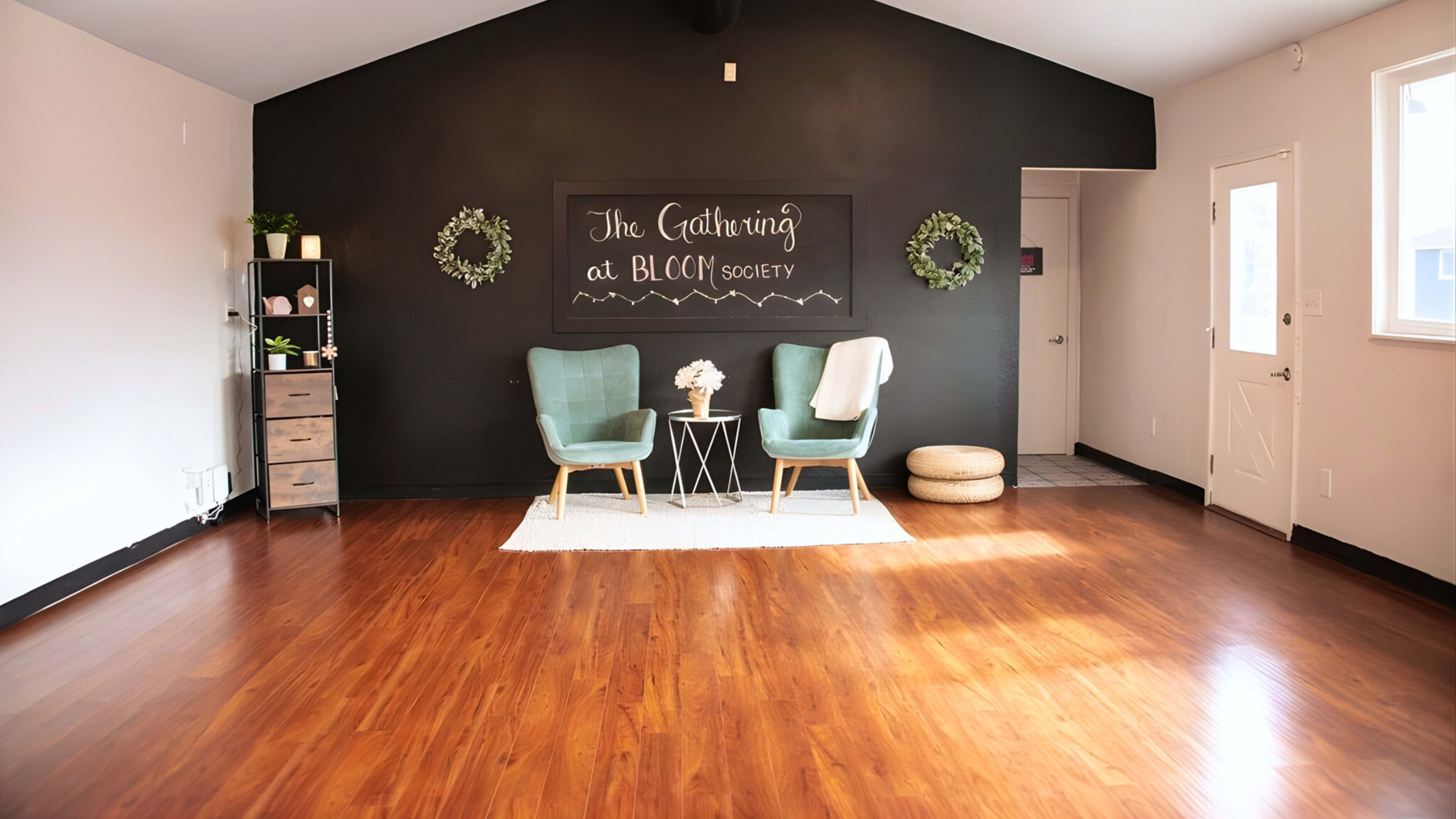 The image shows a spacious, polished room with two green chairs facing a small table, decorated with a floral arrangement, against a black wall featuring the words "The Gathering at BLCC Society."
