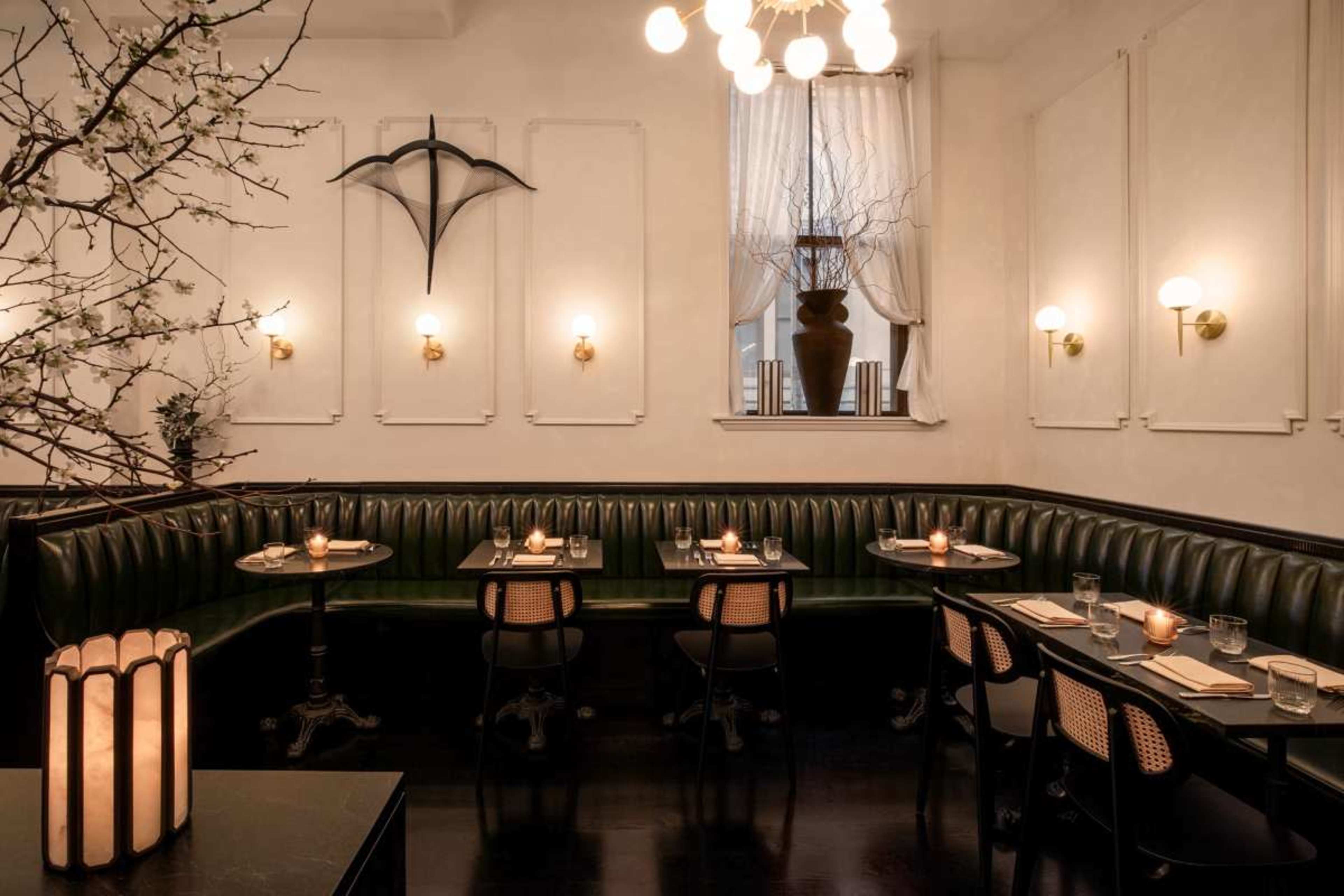 The image shows a restaurant interior featuring a curved green banquette, black tables, and elegant lighting fixtures.