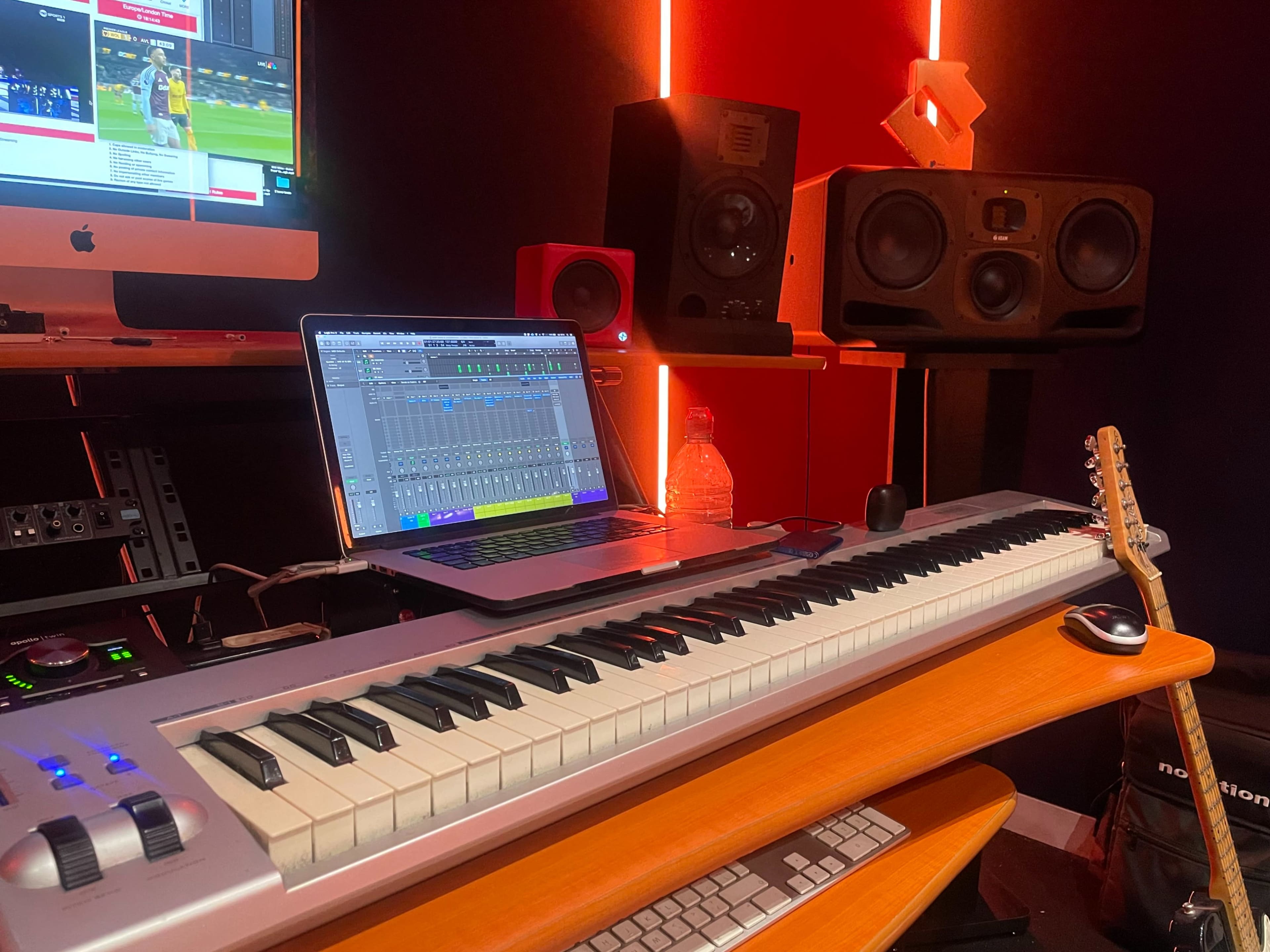 A keyboard, laptop, and audio speakers are arranged on a desk in a music production studio.