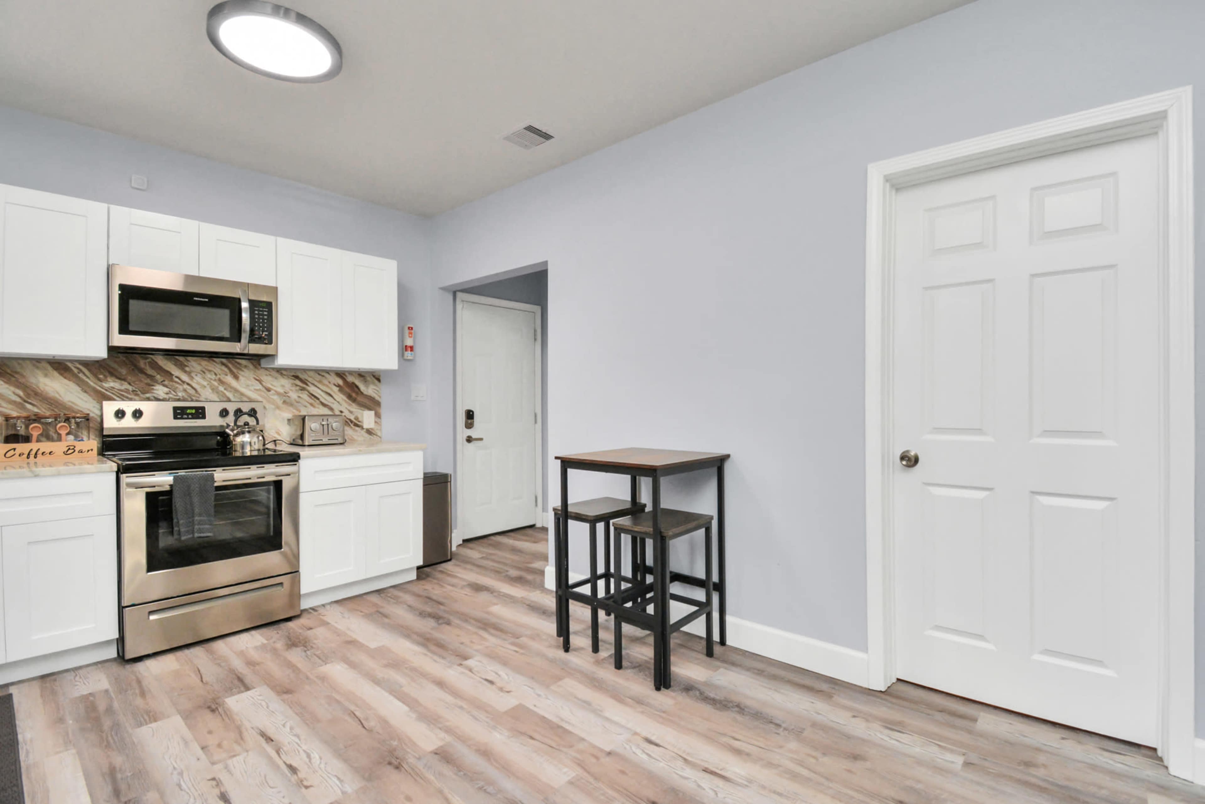 A modern kitchen features stainless steel appliances, white cabinetry, and a small dining table with two chairs against a light-colored wall.
