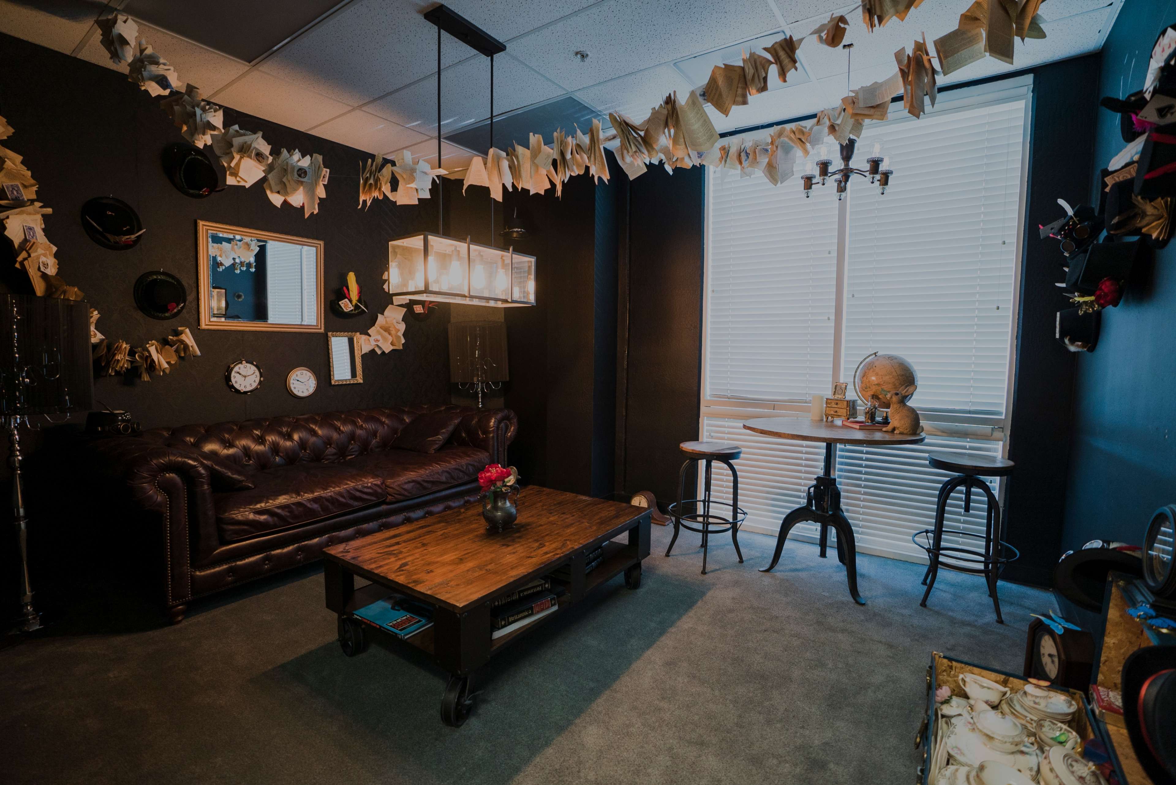 A stylish office space with a leather sofa, a wooden coffee table, and a small round dining table near a window, adorned with decorative paper and hanging hats.