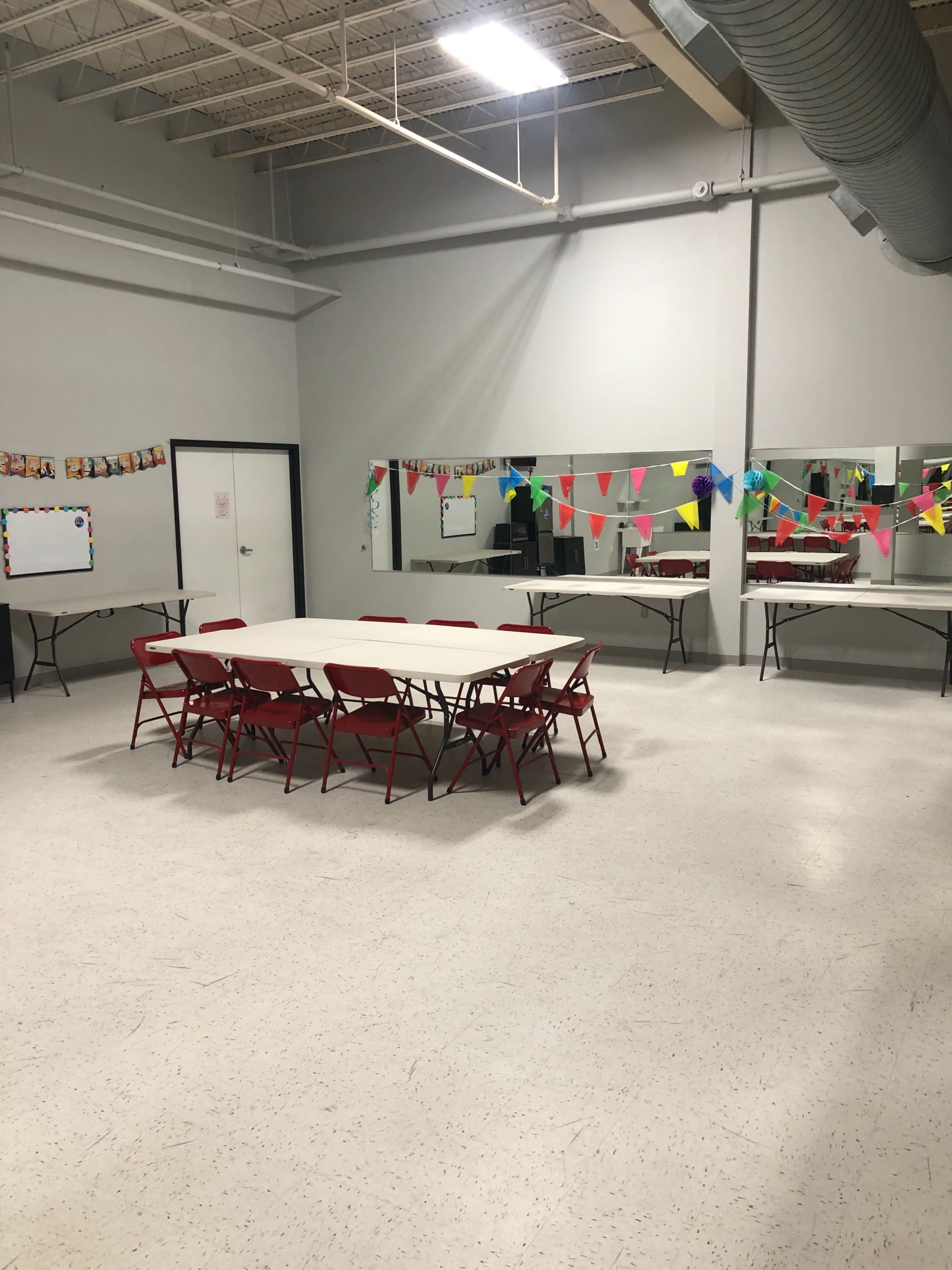 The image shows a spacious meeting room with a central table surrounded by red chairs and decorated with colorful banners and mirrors on the walls.
