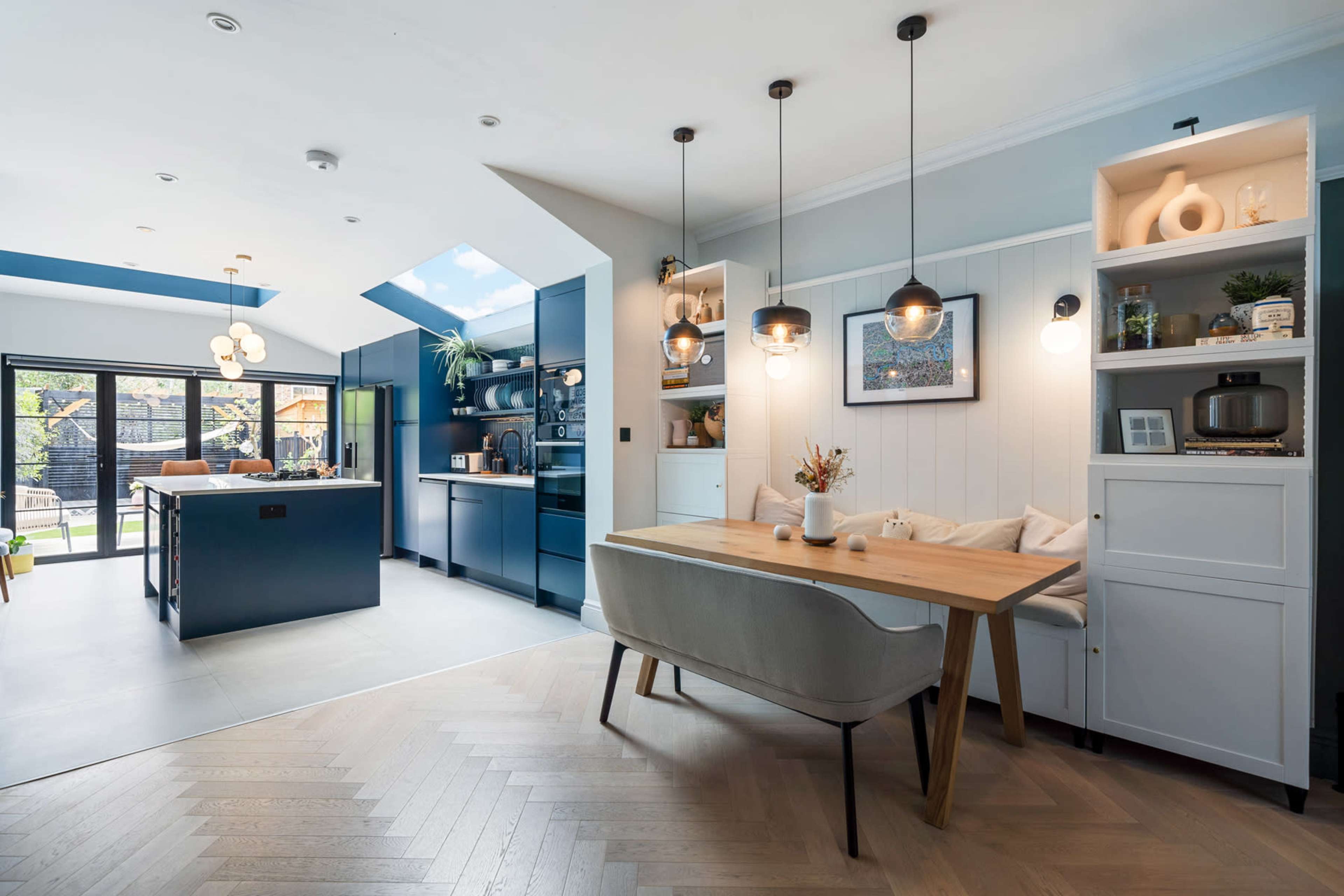 A modern kitchen and dining area features an island with bar seating, suspended light fixtures, and a large window that provides natural light.
