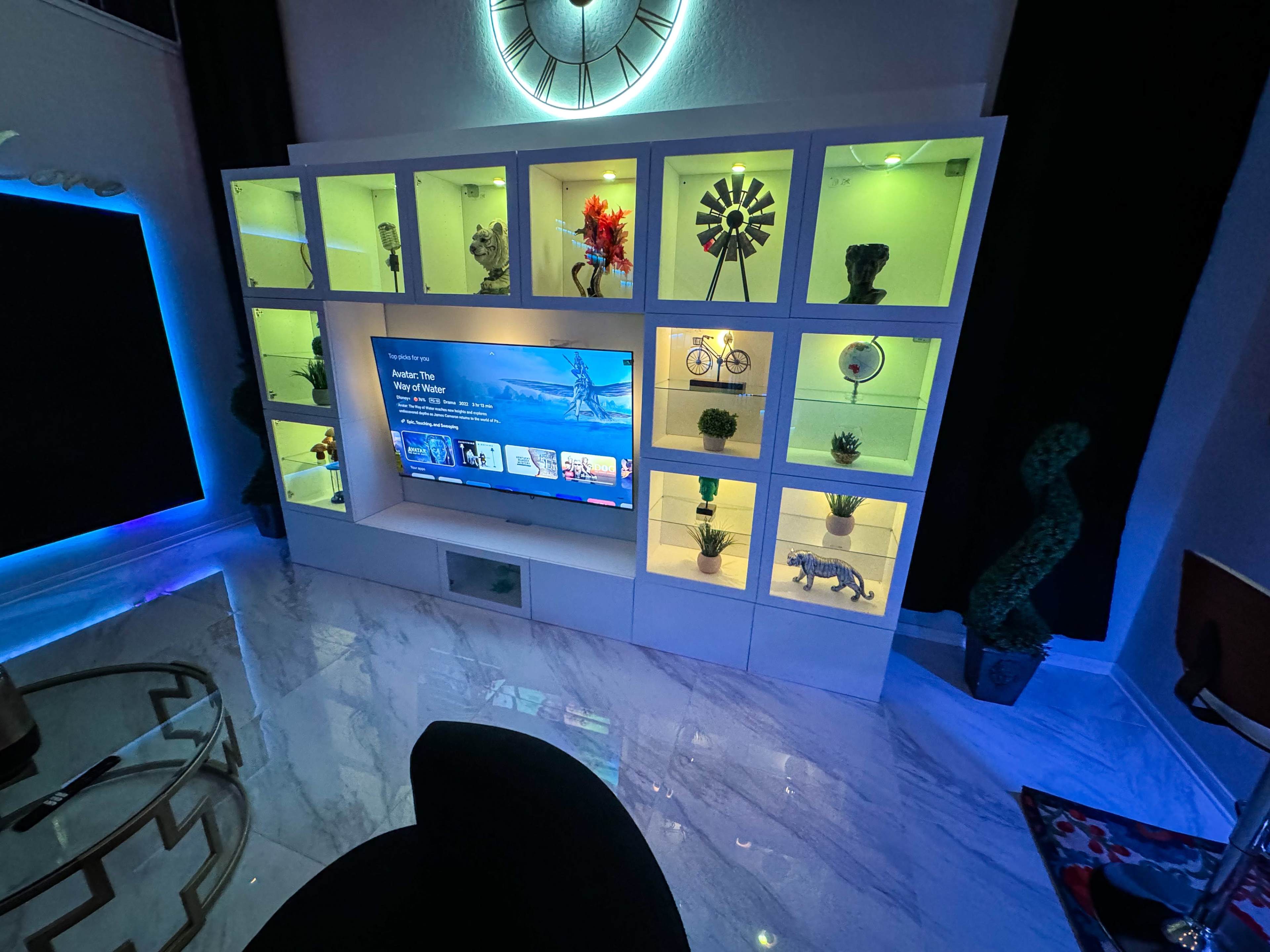 A modern display cabinet with illuminated shelves showcasing decorative items, a television in the center, and a marble floor.
