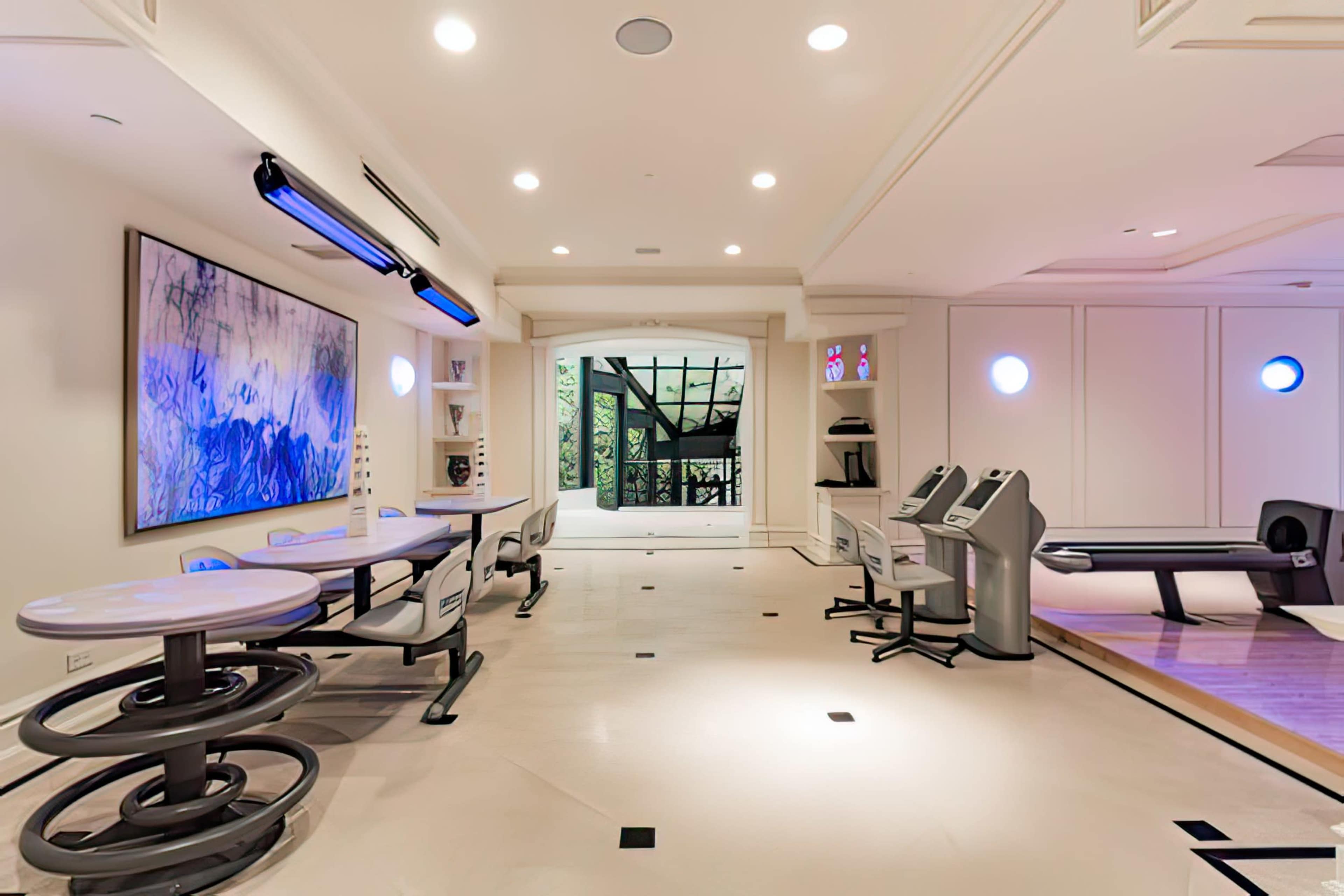 A modern fitness room with exercise equipment, a large wall-mounted artwork, and a view of a glass door leading to an outdoor area.