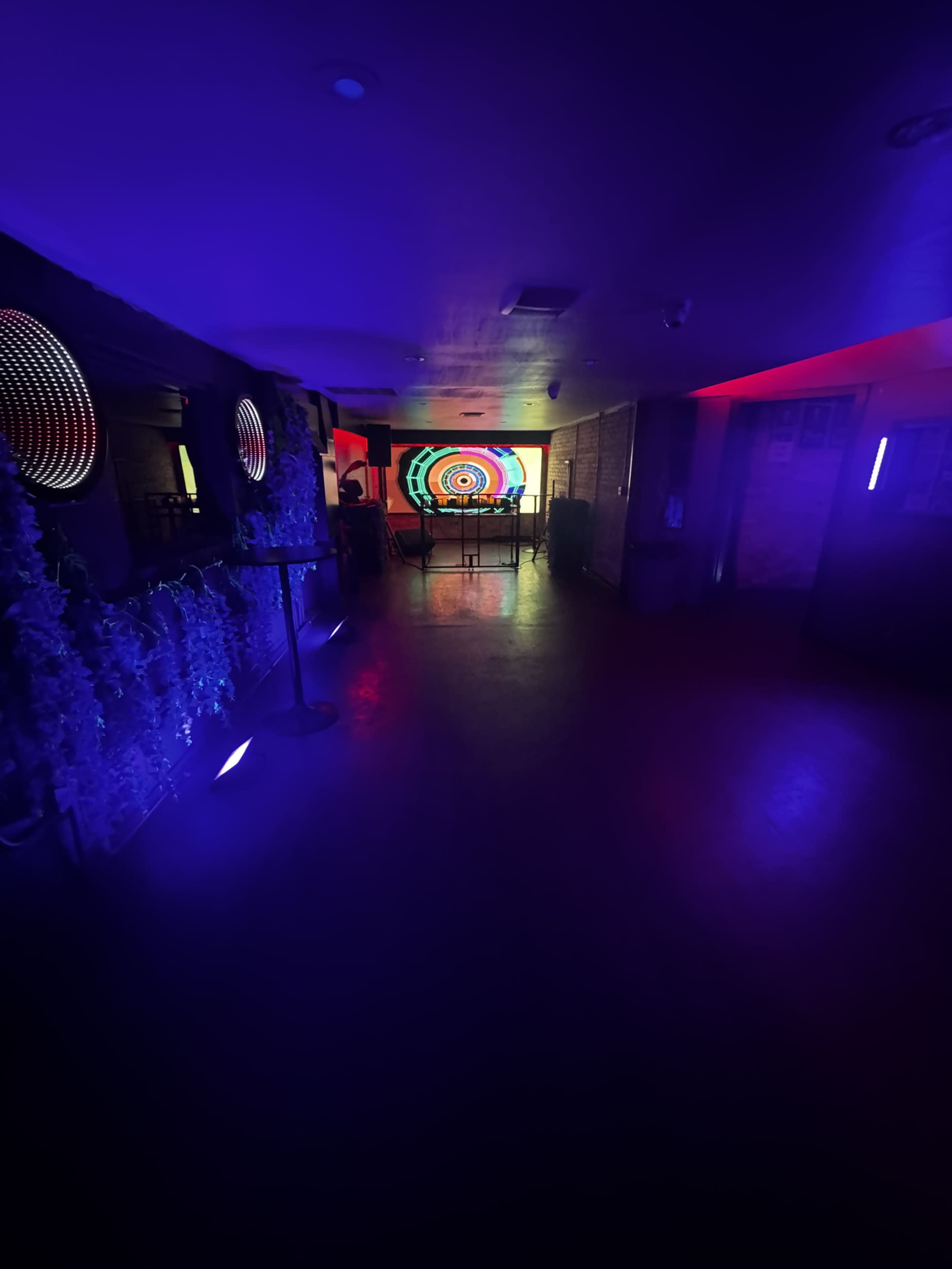 The image shows a dimly lit hallway with colorful lighting, leading to a room featuring a circular patterned projection on the wall.