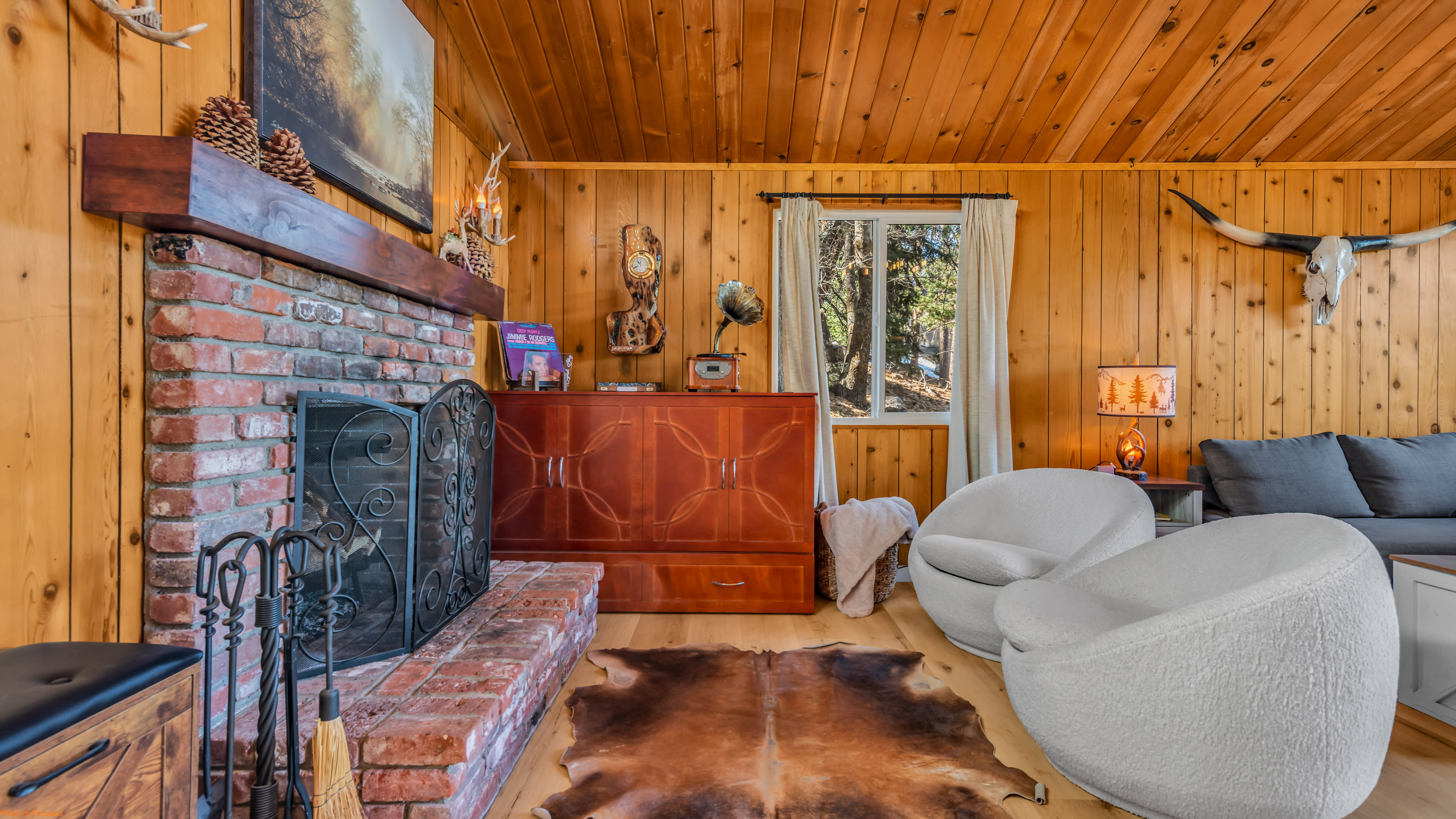 The cozy living room features a brick fireplace, a wooden wall, and modern furniture, including two round chairs and a wooden cabinet.