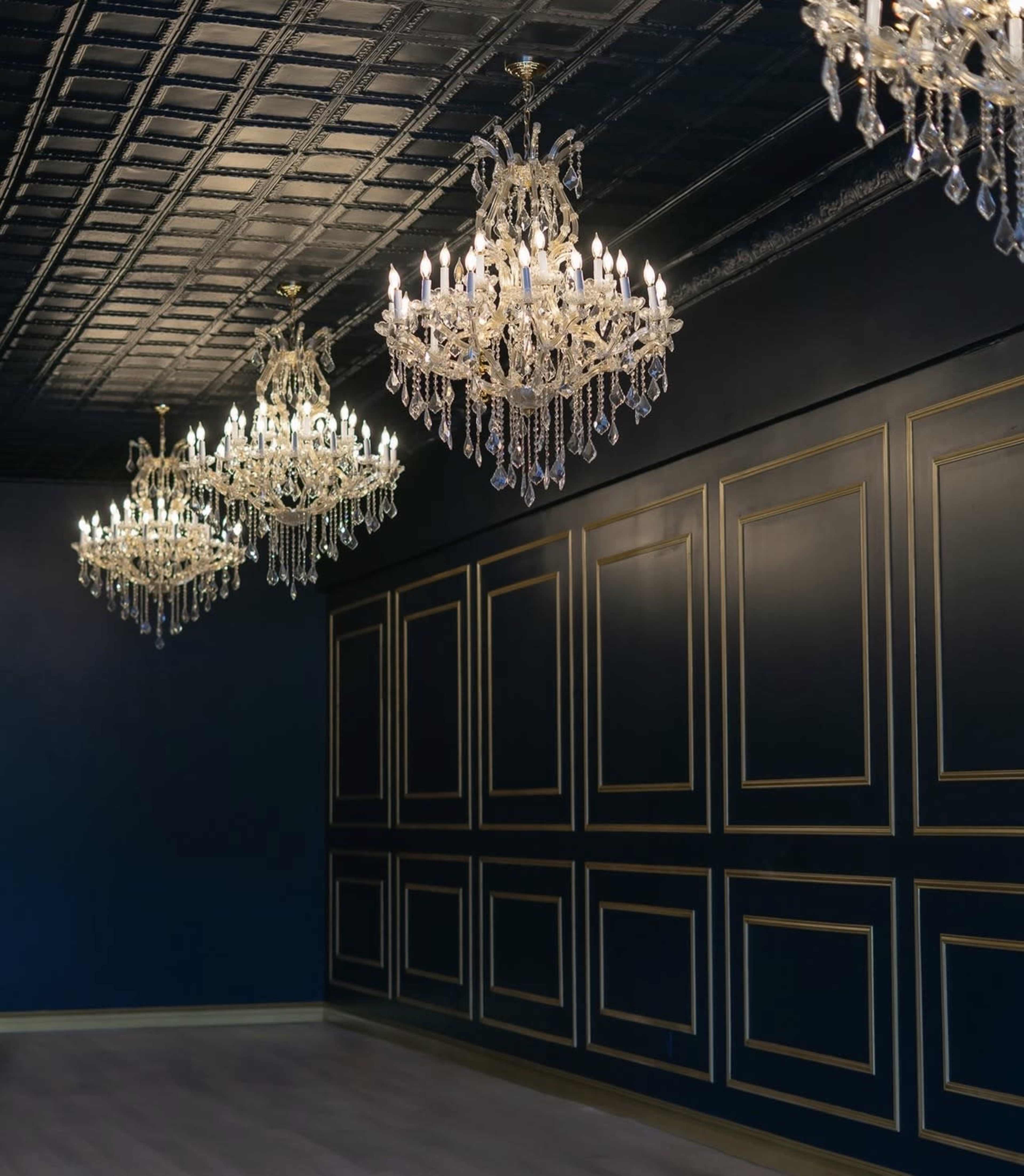 The image shows a room with a dark blue wall and several ornate chandeliers hanging from a ceiling with a patterned design.
