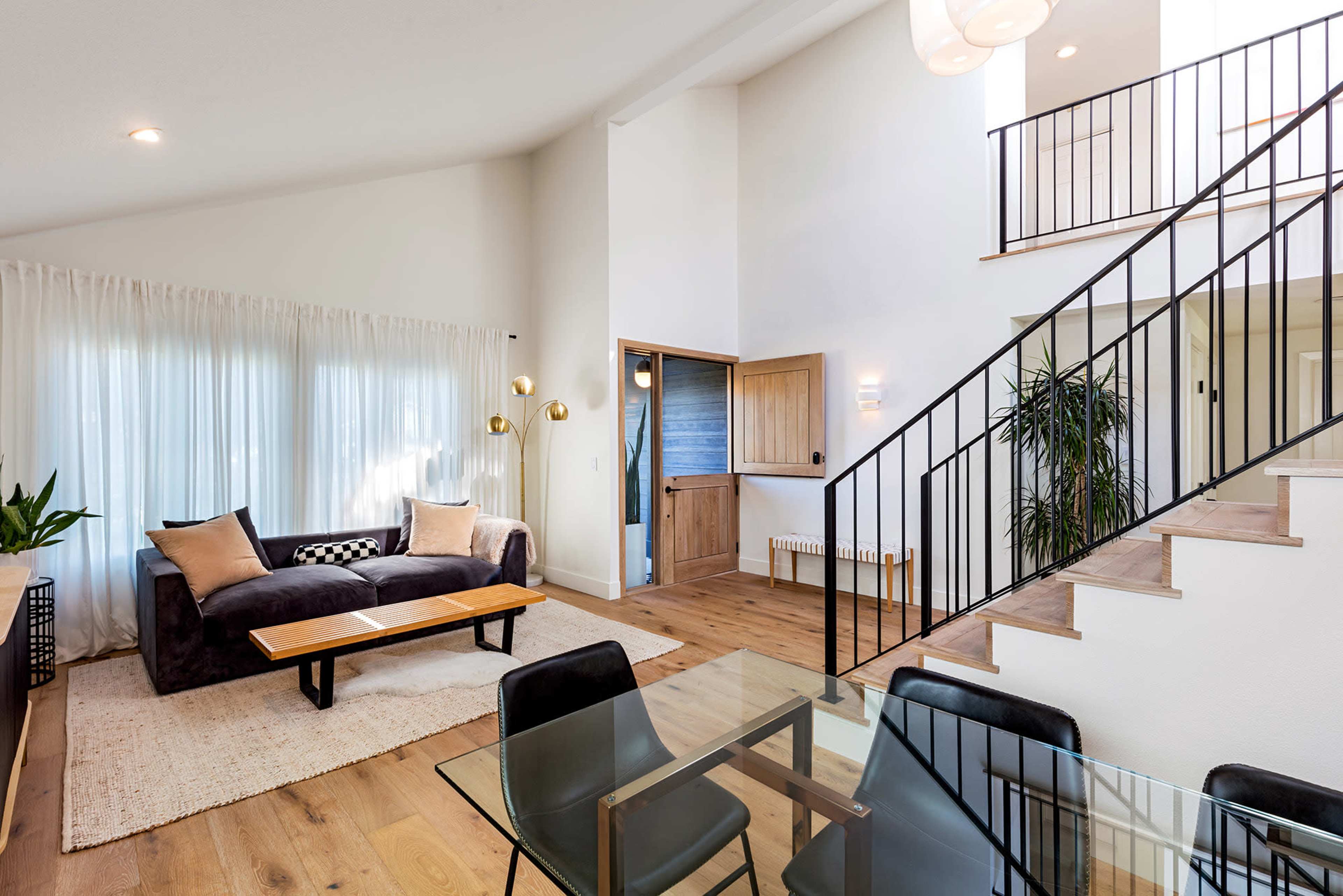 A modern living room with a black couch, a wooden coffee table, a glass dining table, and a staircase leading to a second floor.