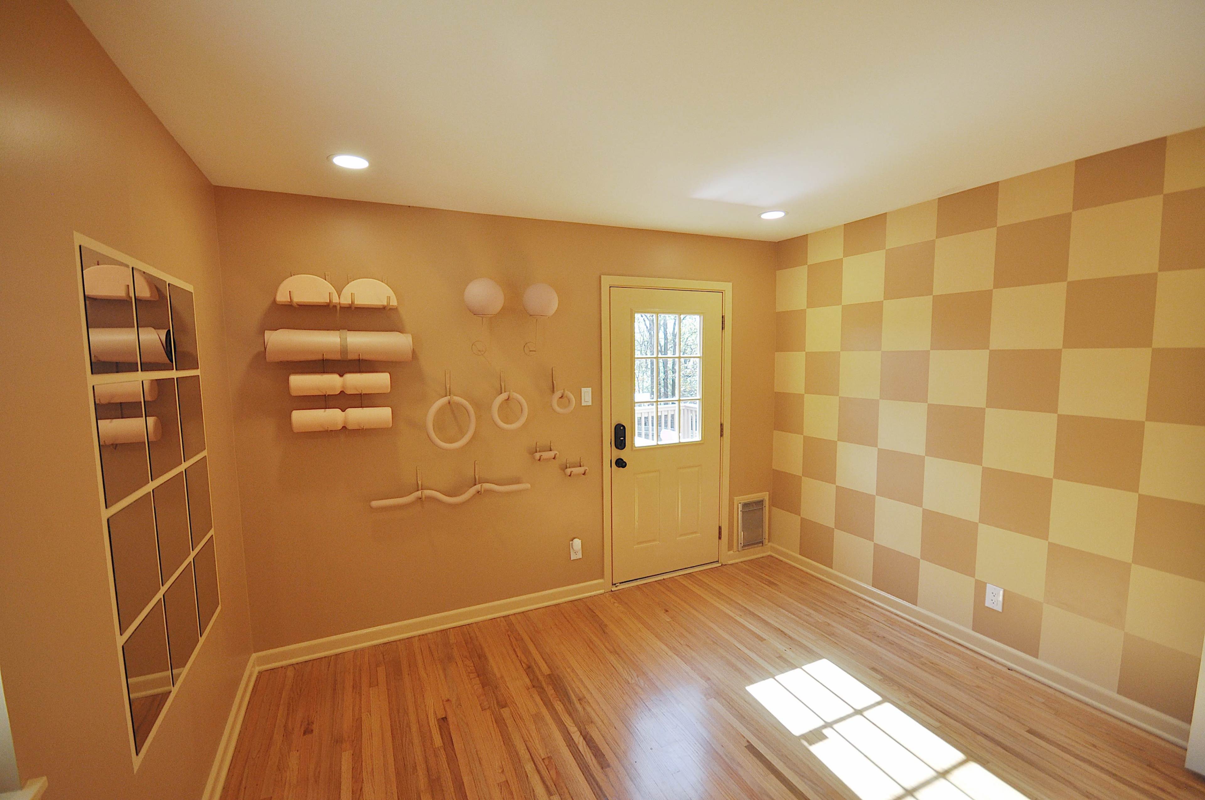 The room features a beige and yellow checkered wall, a door leading outside, and several decorative wall-mounted items alongside a large mirror.