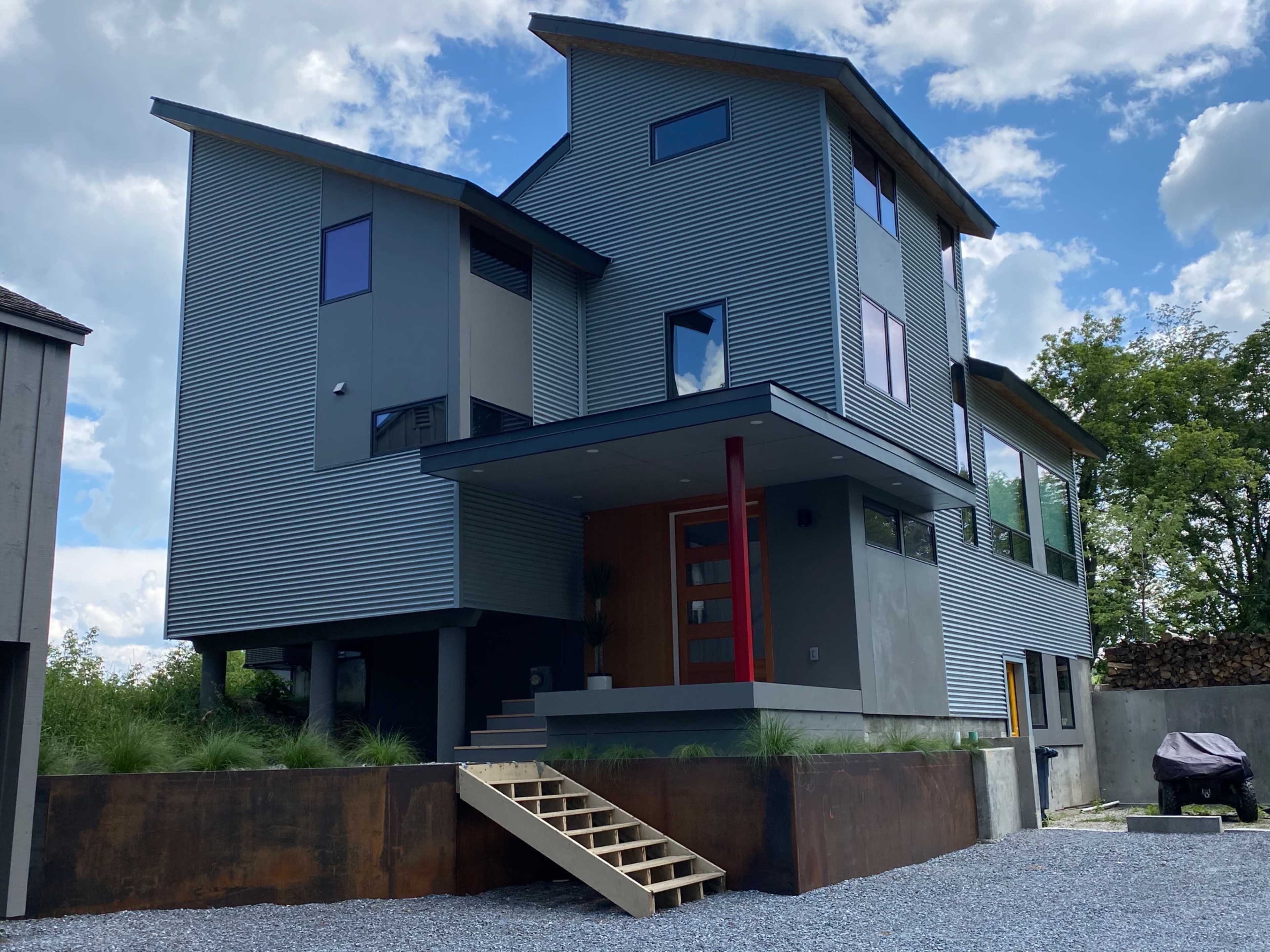 A modern three-story house with angular architecture features a row of steps leading to a wooden front door and large windows.