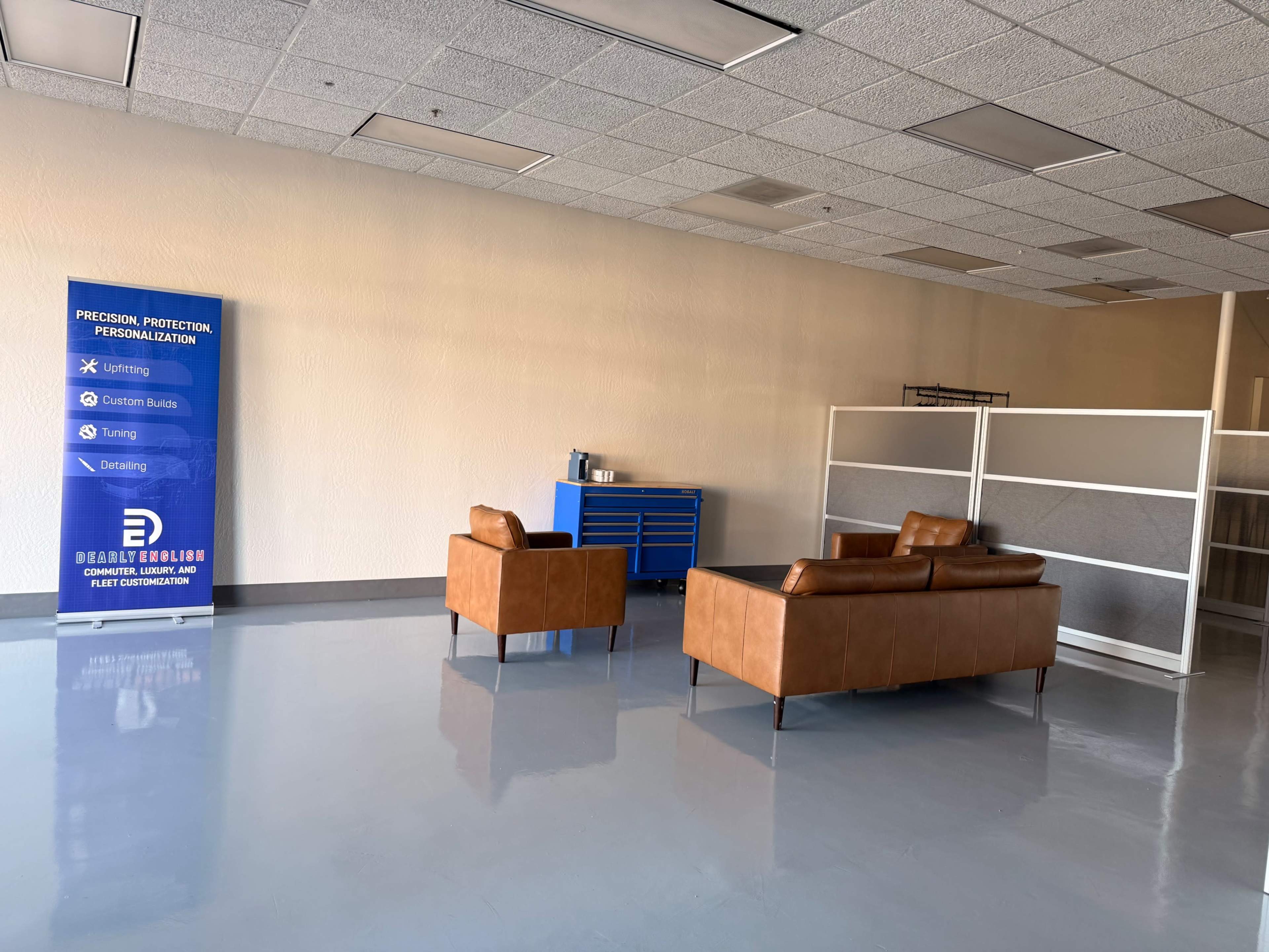 The image shows a sparsely furnished office space with two brown leather sofas, a blue tool cabinet, and a sign promoting personalized services on one wall.
