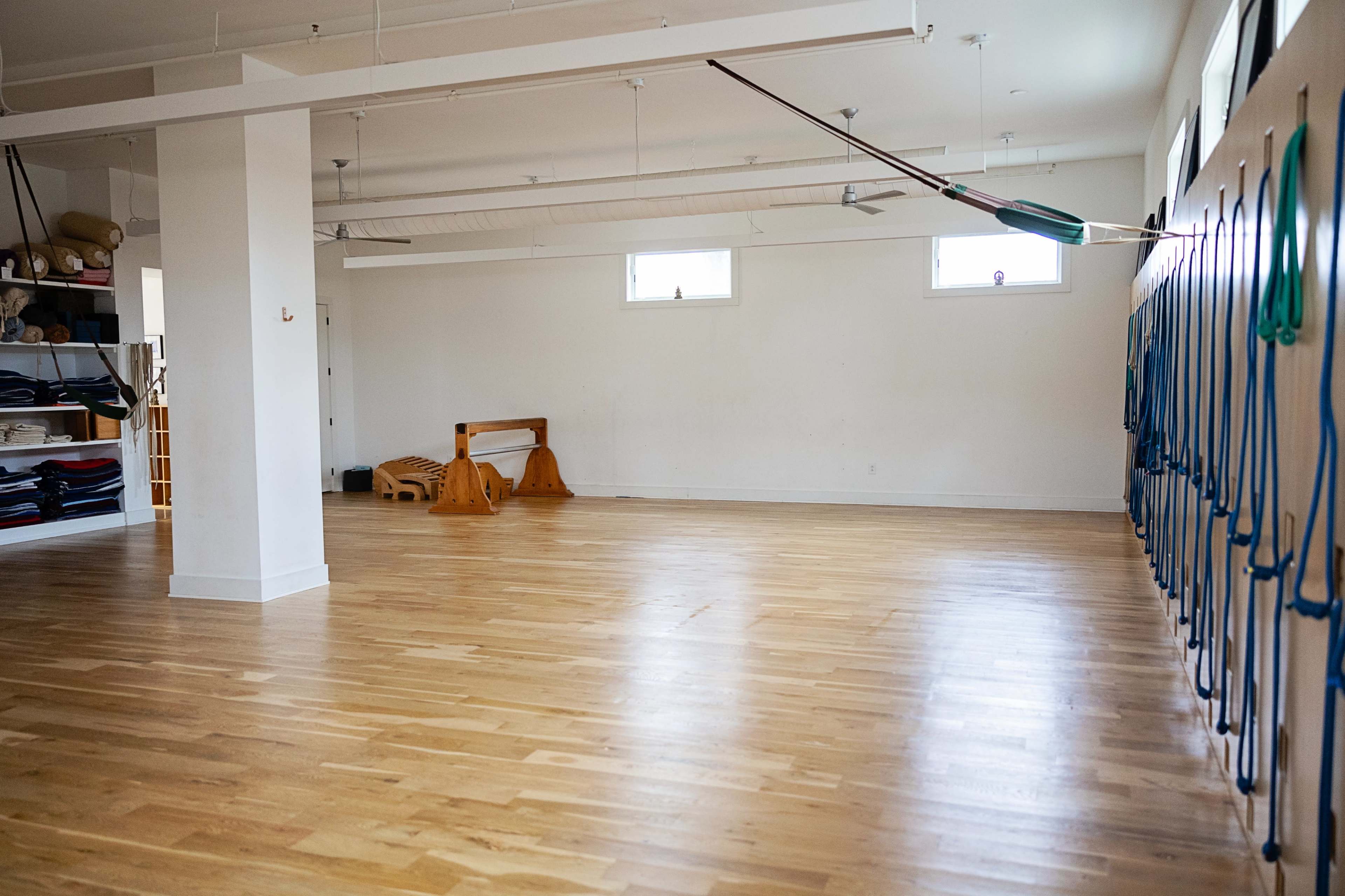 A spacious, empty room with wooden flooring and exercise equipment along the walls.