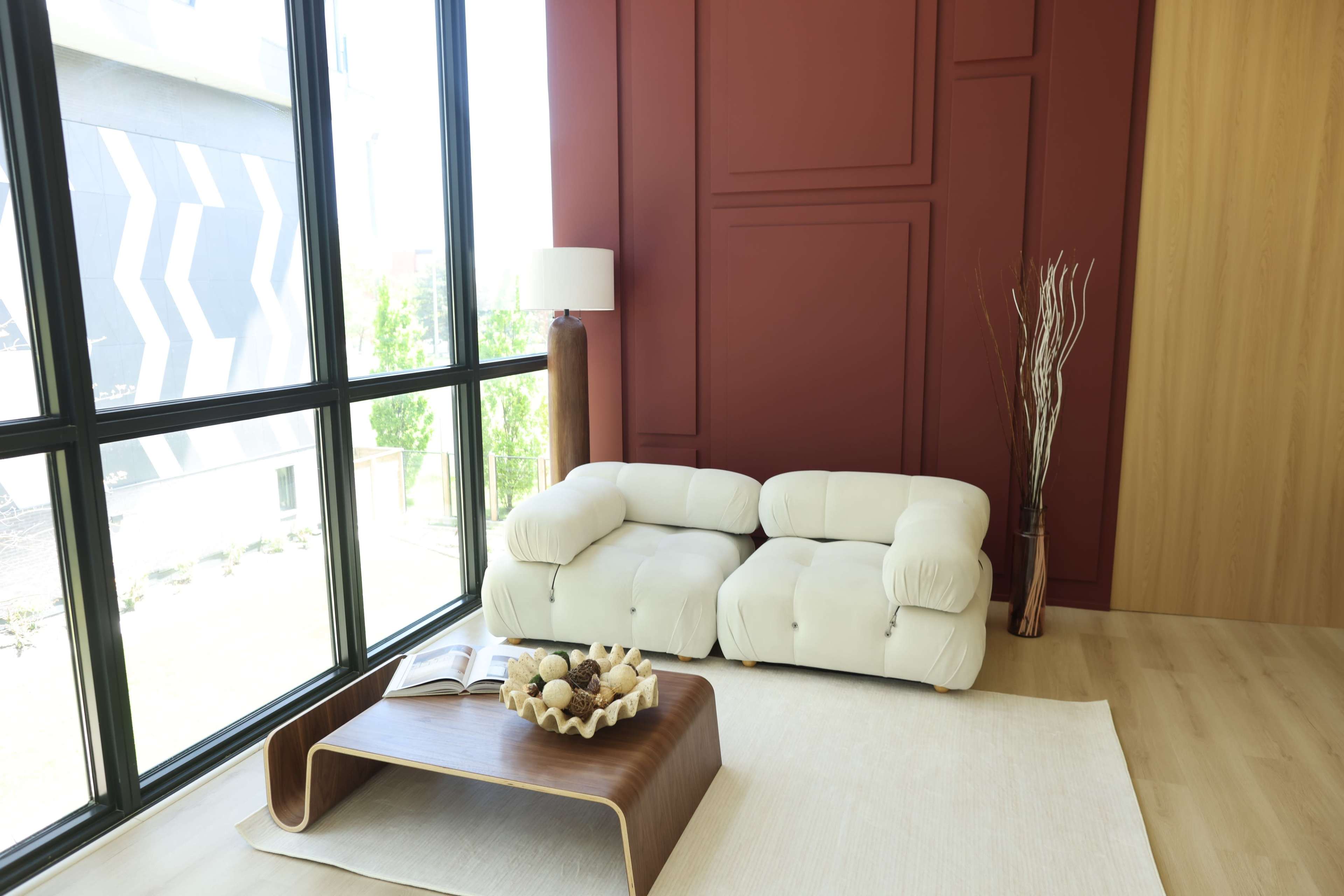 The image features a modern interior with a white sofa, a wooden coffee table, and large windows allowing natural light to flood the space.
