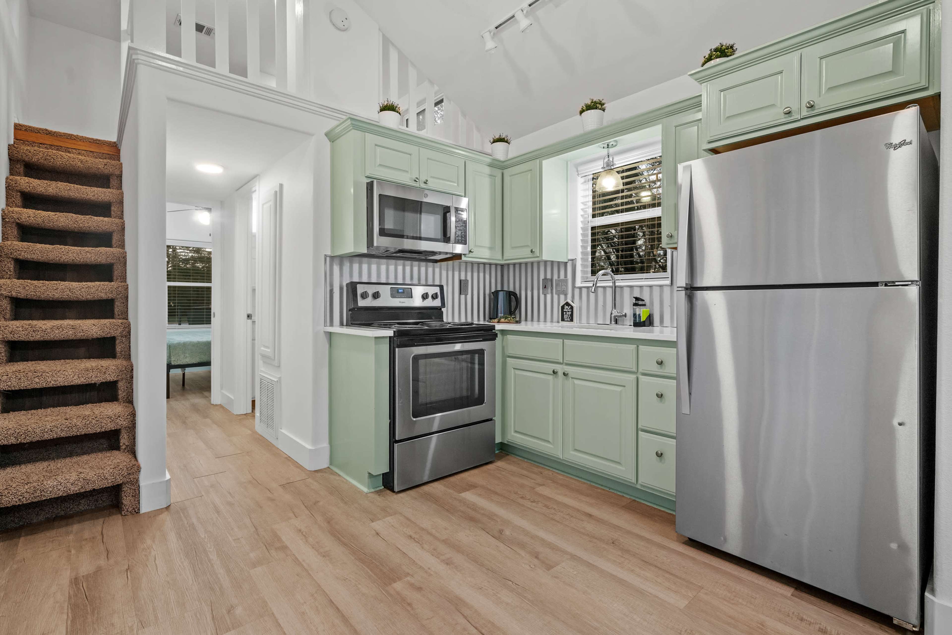 A kitchen with green cabinetry, stainless steel appliances, and a staircase leading to an upper level.