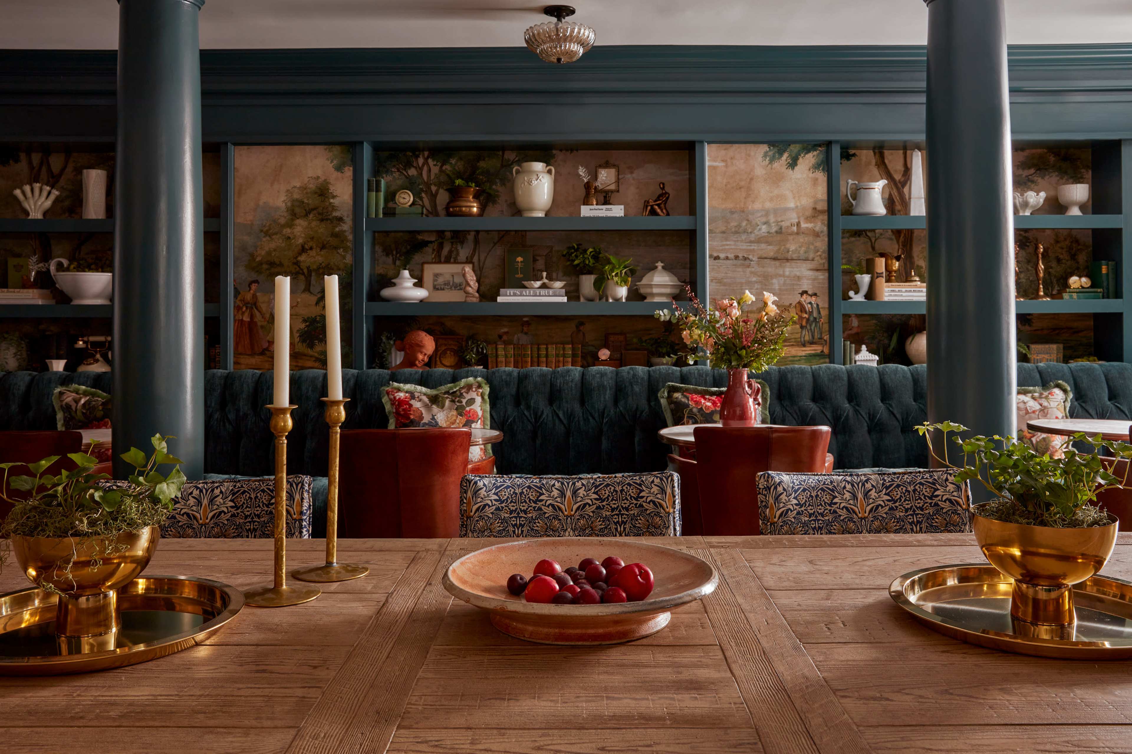 A dining area features a wooden table with decorative bowls and candles, surrounded by upholstered chairs and shelves displaying various decor items.