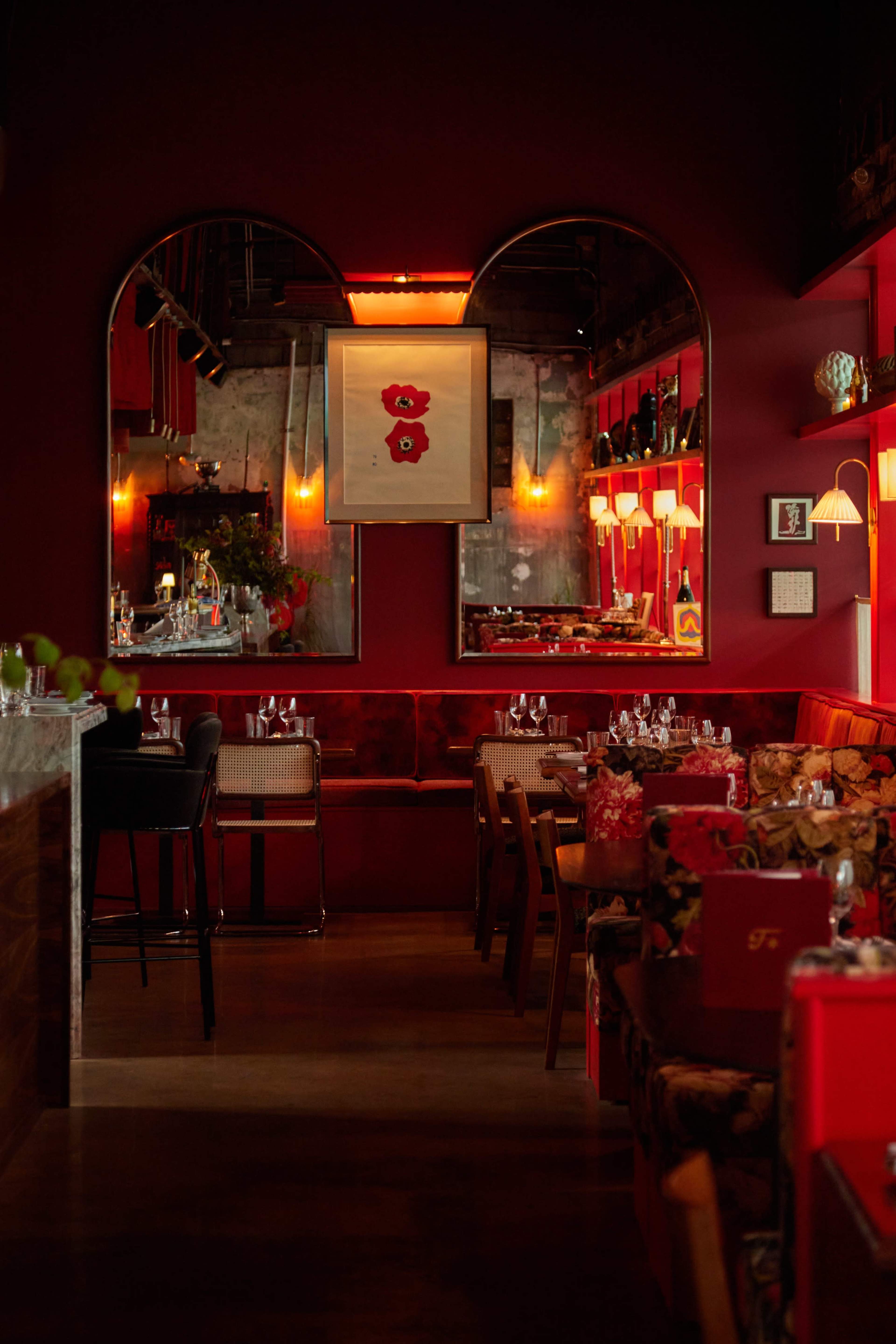 The image shows a dimly lit restaurant featuring dark red walls, vintage decor, and tables set with glassware.