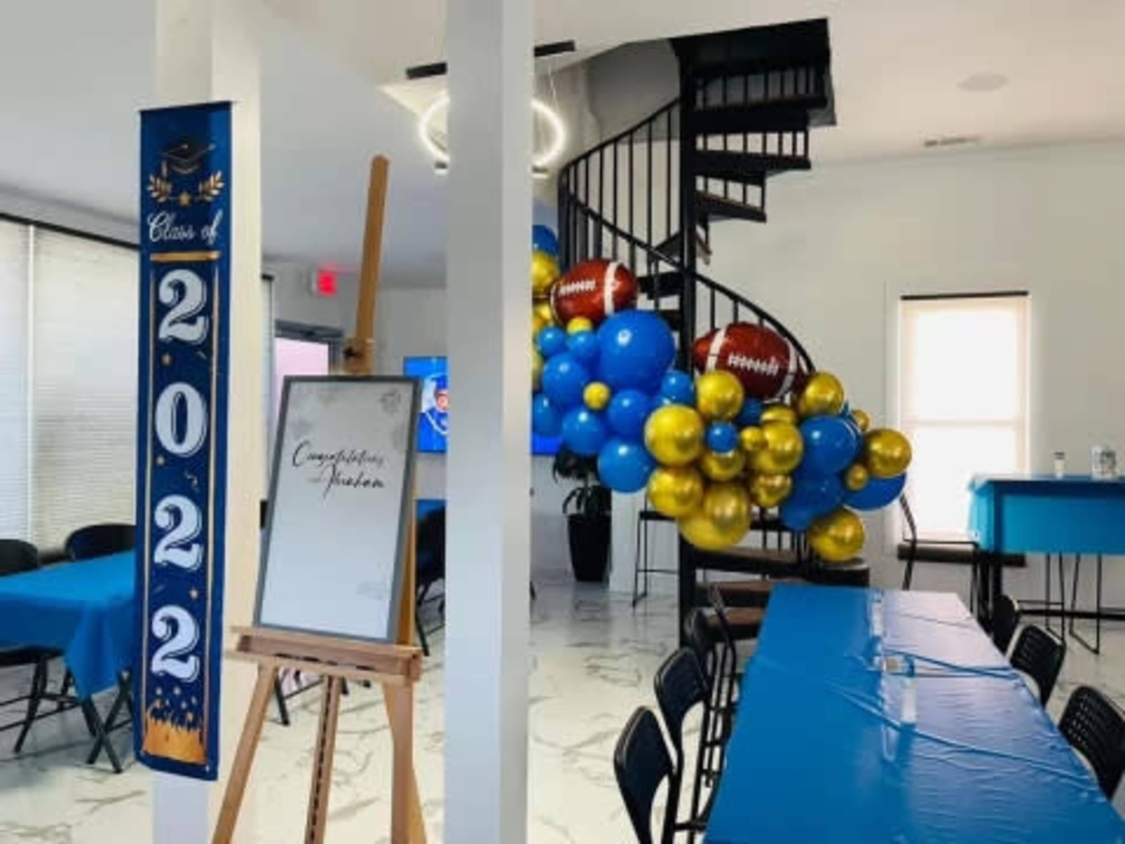 A decorated room features blue and gold balloons, a "Congratulations" sign on an easel, and tables set for a celebration honoring the Class of 2022.
