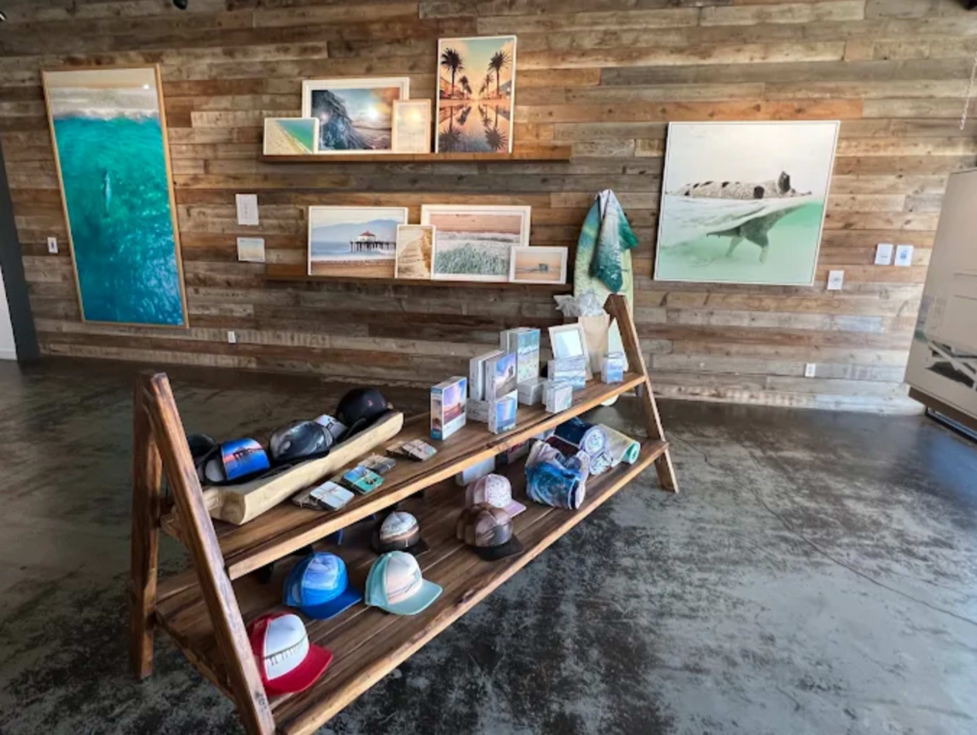The image shows a retail space featuring wooden shelves displaying framed photographs and various merchandise, including hats and decorative items, arranged on a rustic wooden display stand.