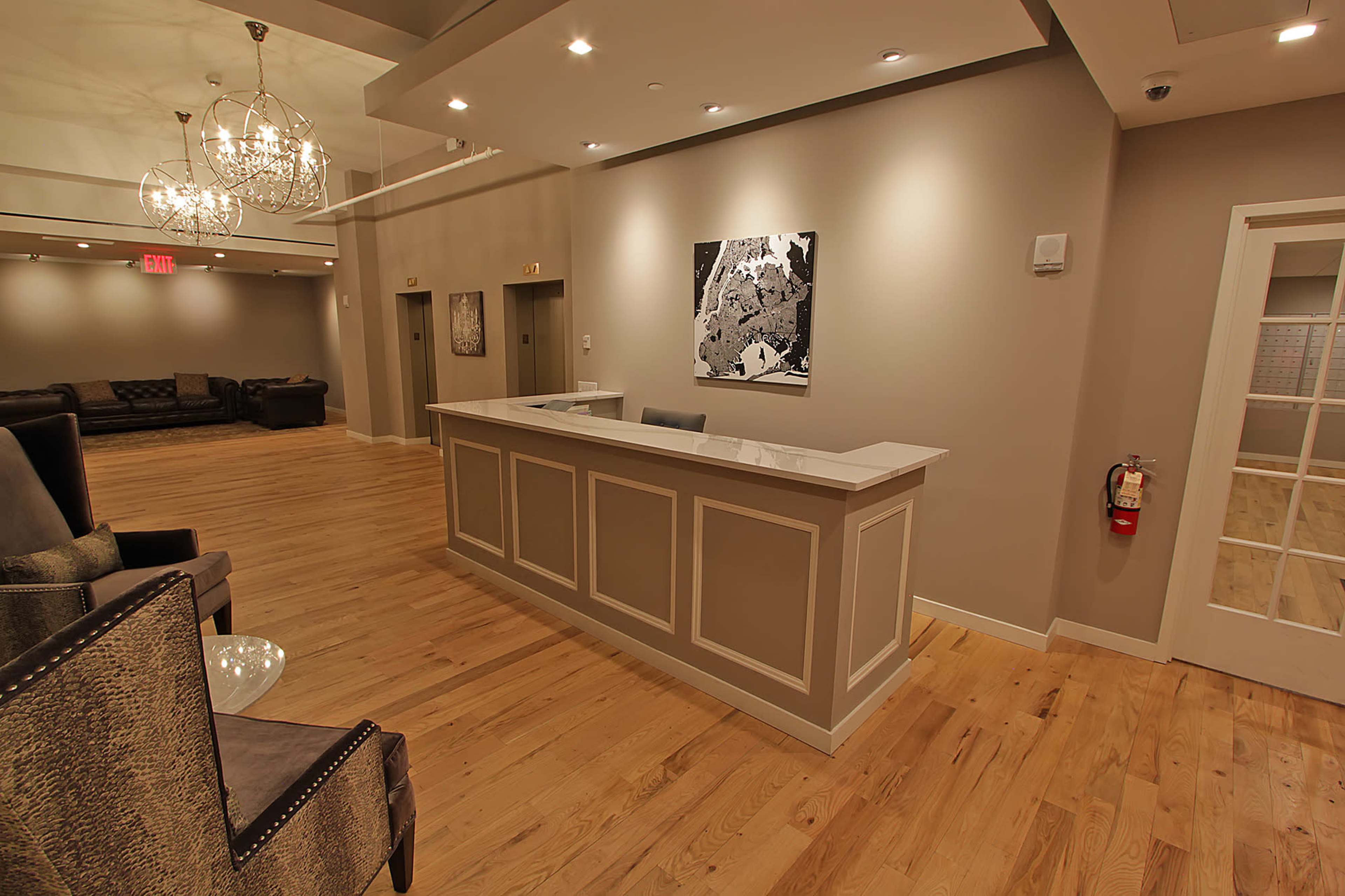 A modern reception area with a front desk, hardwood flooring, and textured walls, illuminated by decorative hanging lights.