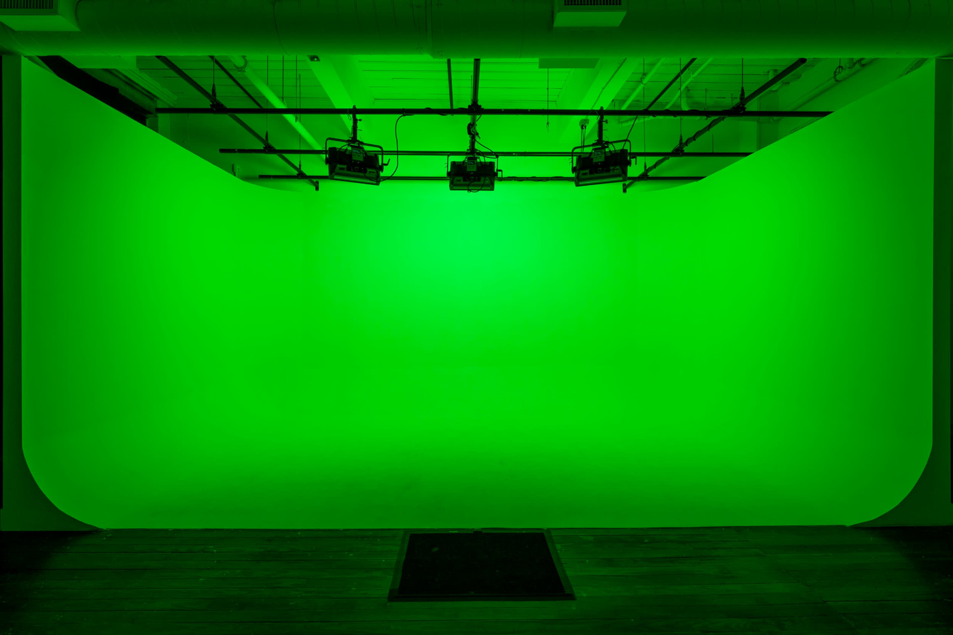 A green screen backdrop illuminated by overhead lights in a studio setting.