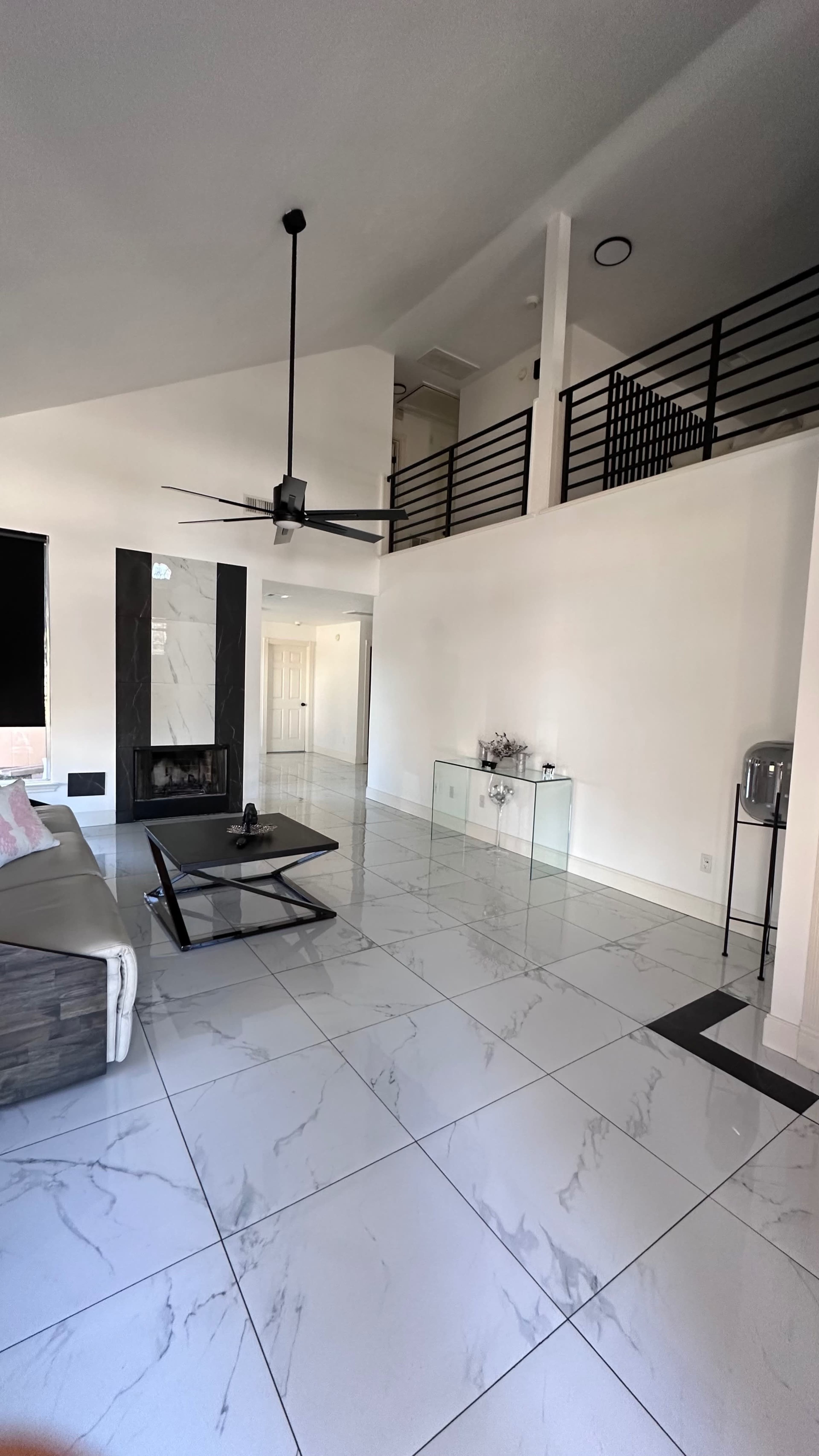 A modern living room featuring a large marble-tiled floor, a fireplace, a ceiling fan, and a staircase leading to a second level.