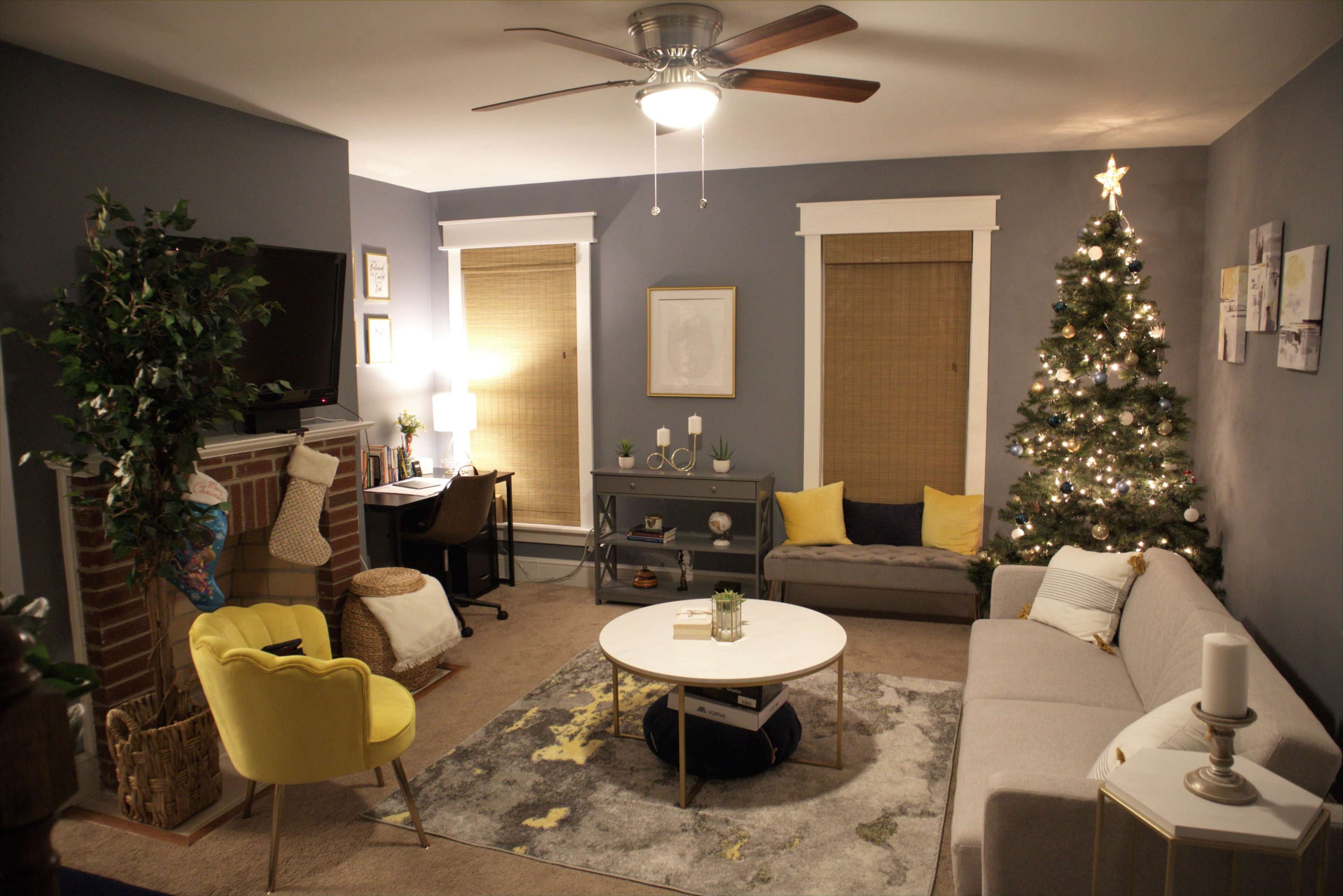 A cozy living room features a Christmas tree, a sofa, a coffee table, and a workspace beside a fireplace.