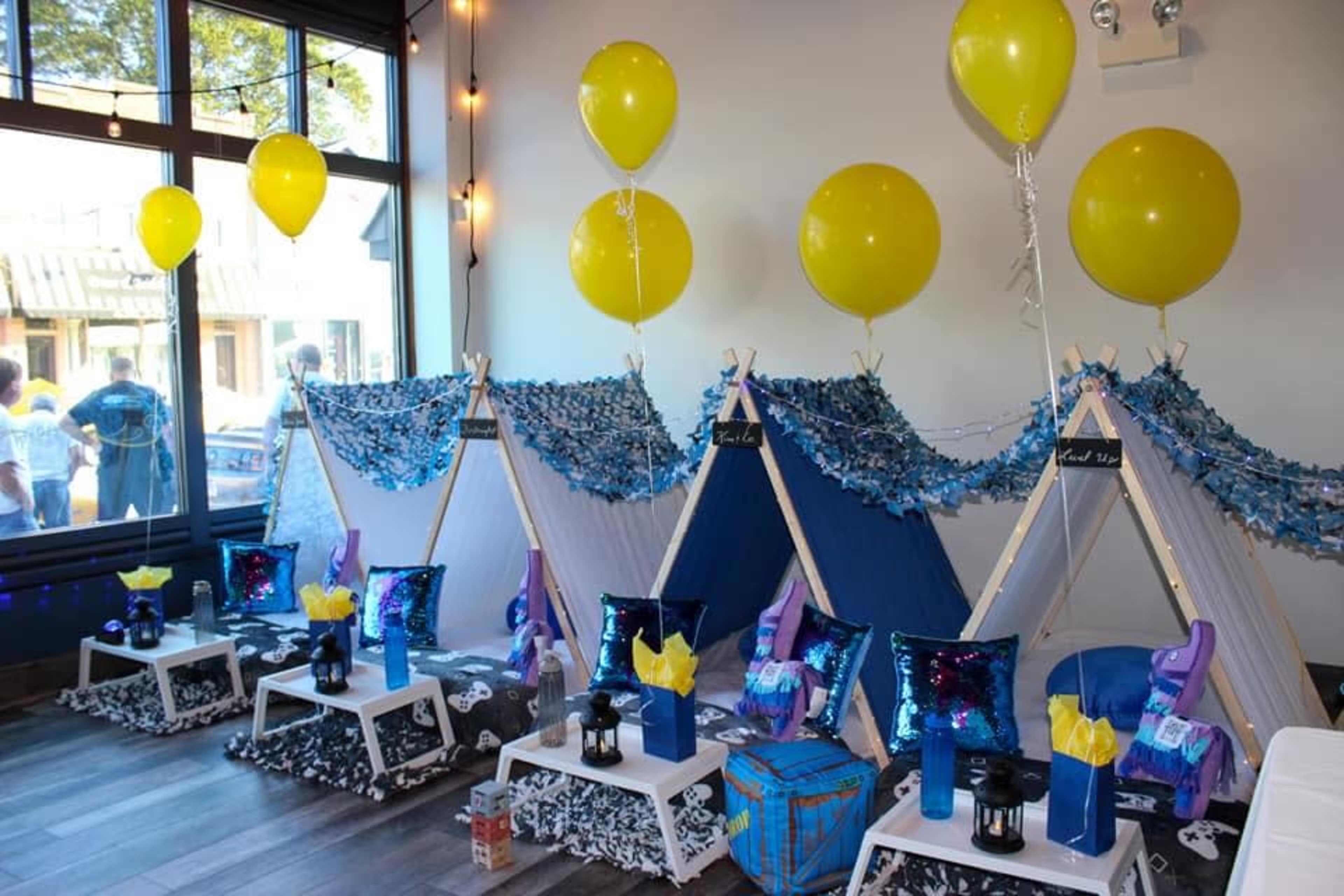 A decorated room with three small teepees set up for a party, surrounded by balloons and colorful cushions.