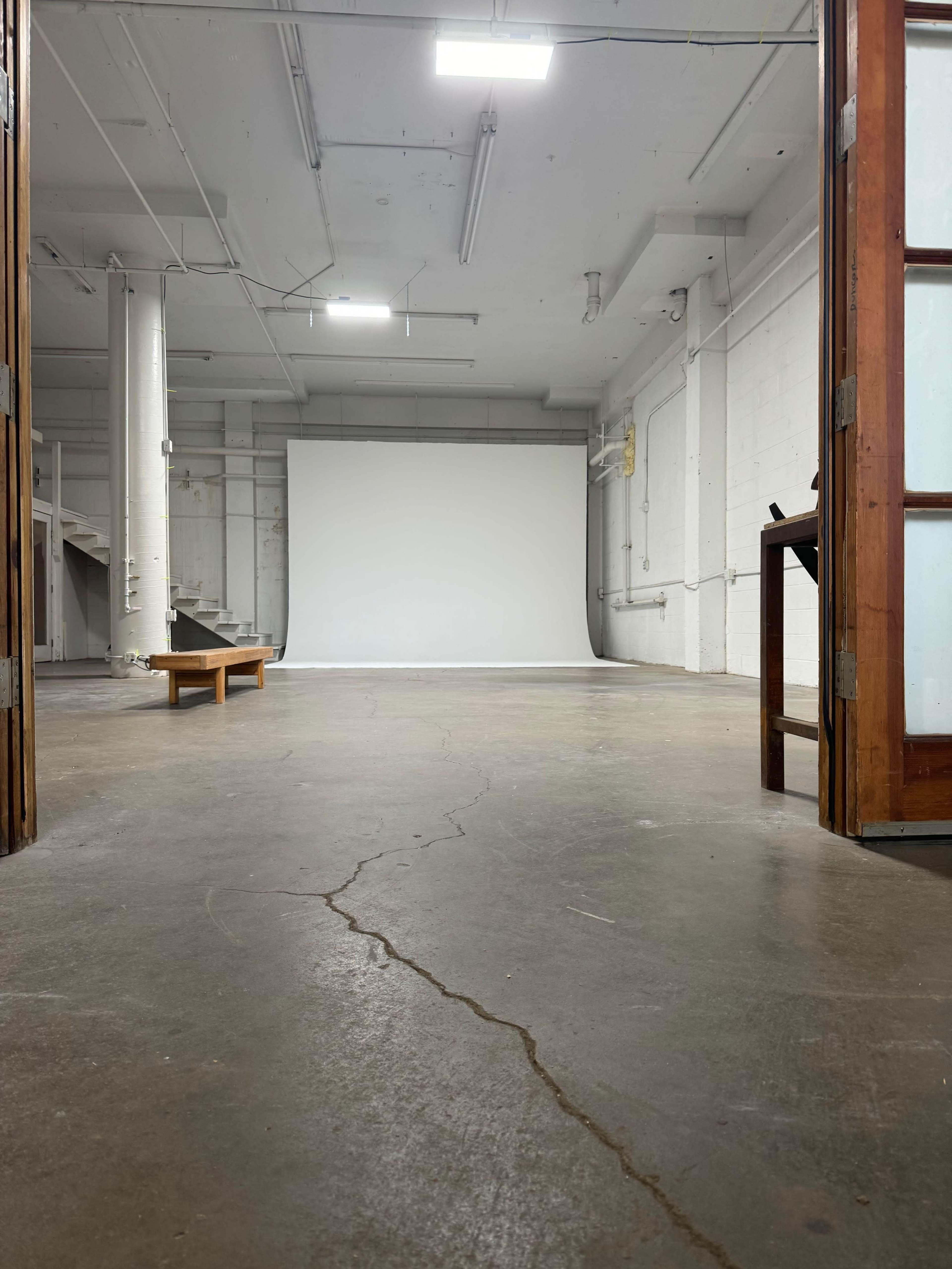 An empty studio space with a blank white backdrop at the far end and a wooden bench in the foreground.