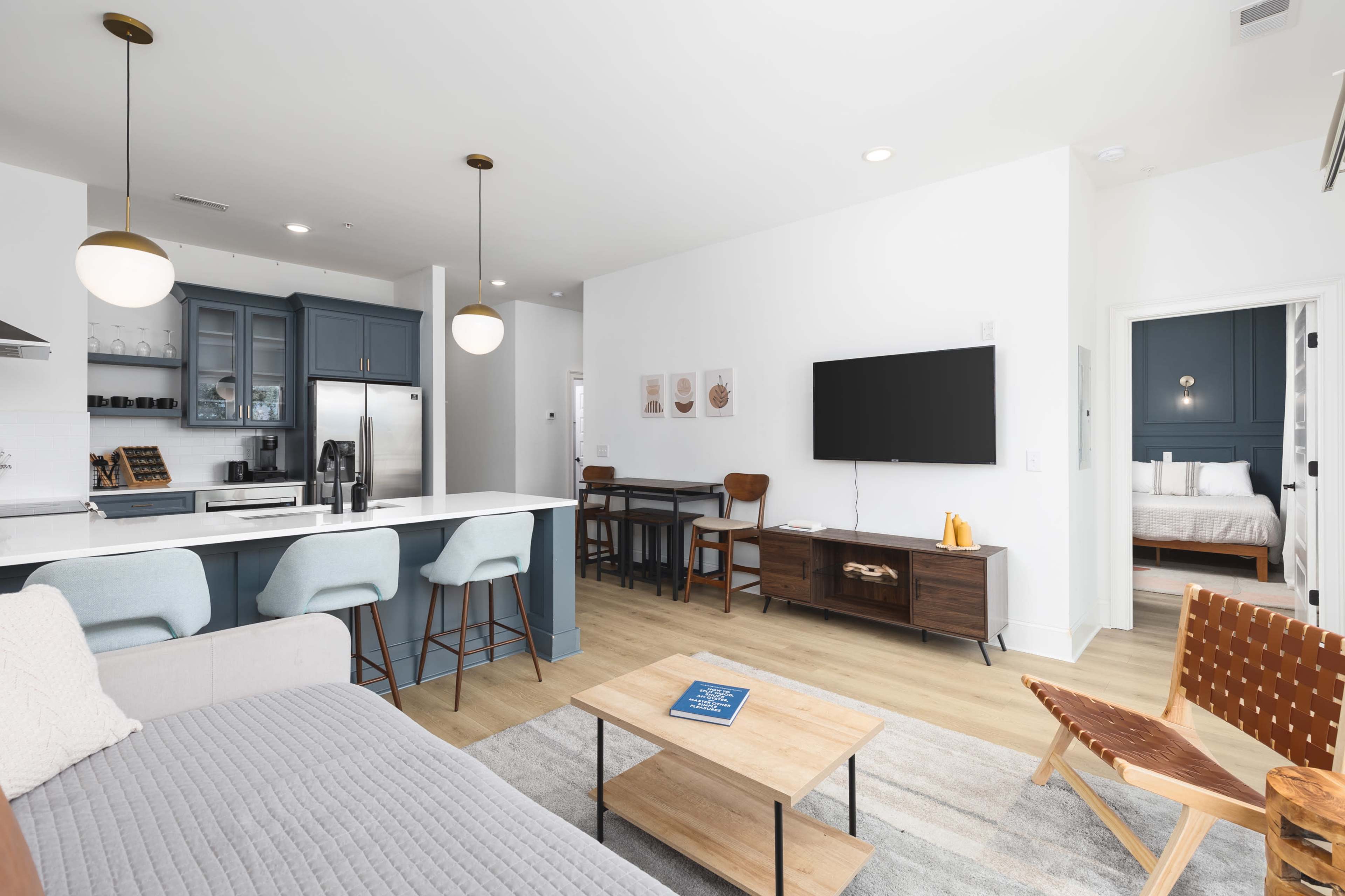 A modern living space features a kitchen with a blue island, a dining area, and a lounge area with a television and a coffee table.