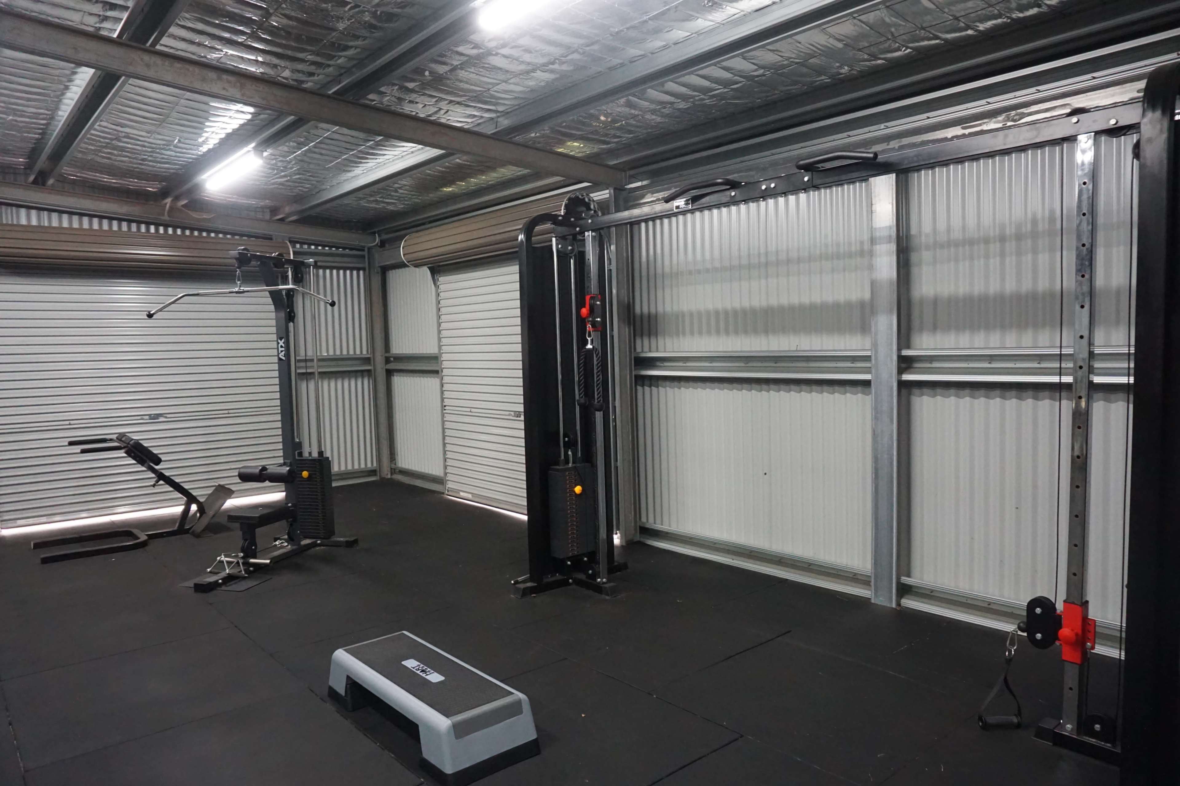 An indoor gym space equipped with exercise machines, including a cable crossover and a weight bench, on a rubberized floor.