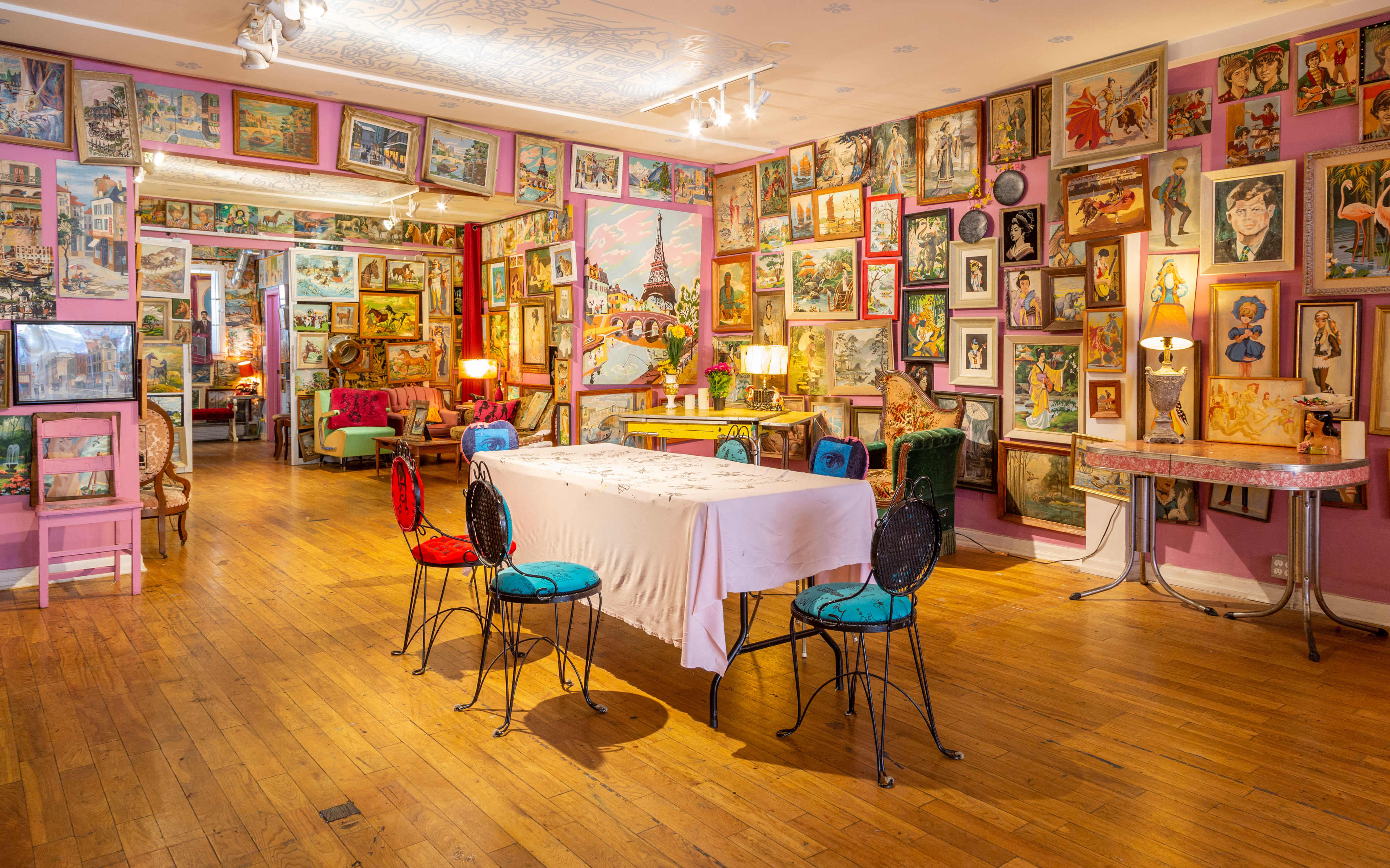 The image shows a colorful gallery-like room filled with framed artworks on the walls and a table with chairs in the center.