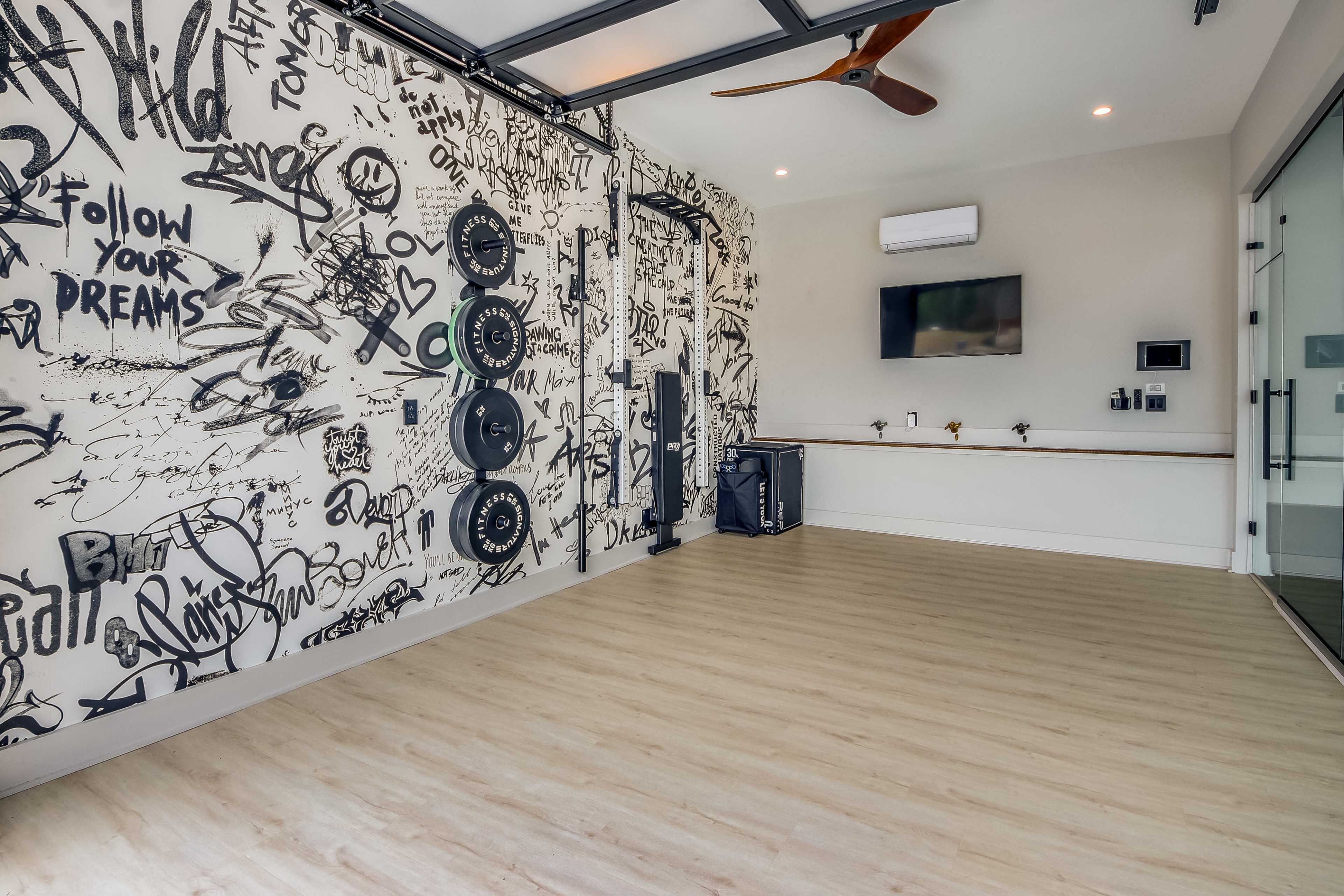 The image shows an exercise room featuring a wall covered in graffiti art, with fitness equipment and a television mounted on the wall.